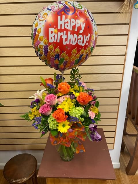 Birthday balloon above a colorful mixed flower arrangement in a glass vase