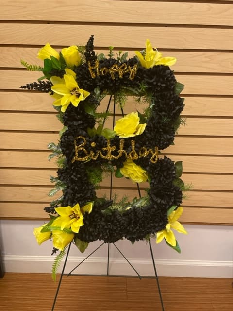 Black and yellow floral standing wreath on an easel with birthday lettering