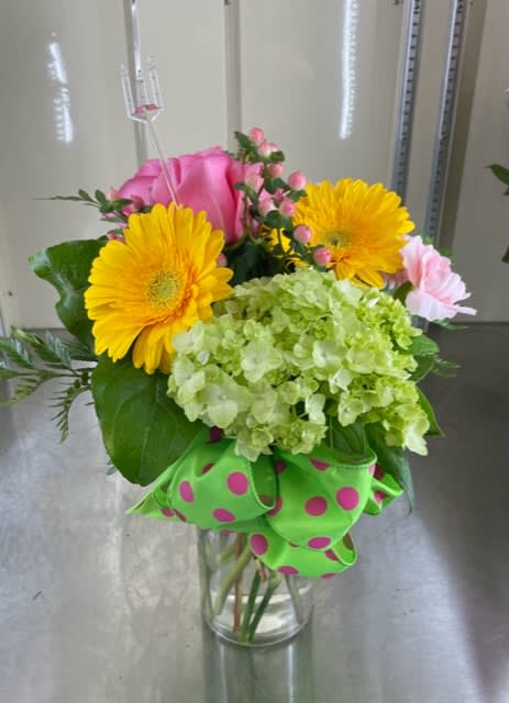 Bouquet of yellow gerbera daisies, pink roses, and green hydrangea in a glass vase