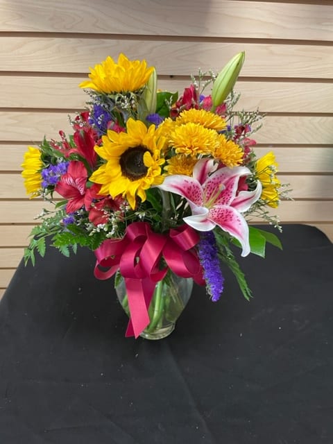 Mixed bouquet with sunflowers, lilies, and a pink ribbon in a glass vase