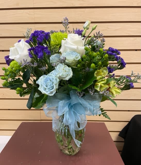 Bouquet of white and pale blue roses with purple filler in a glass vase