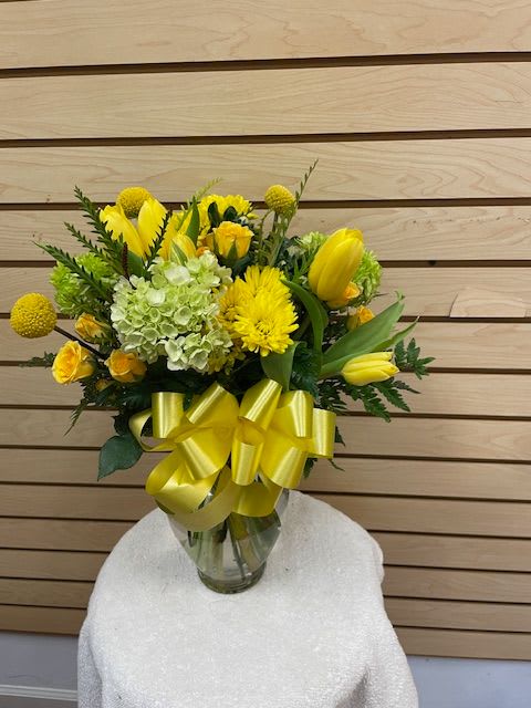 Yellow floral bouquet in a glass vase with a large yellow ribbon
