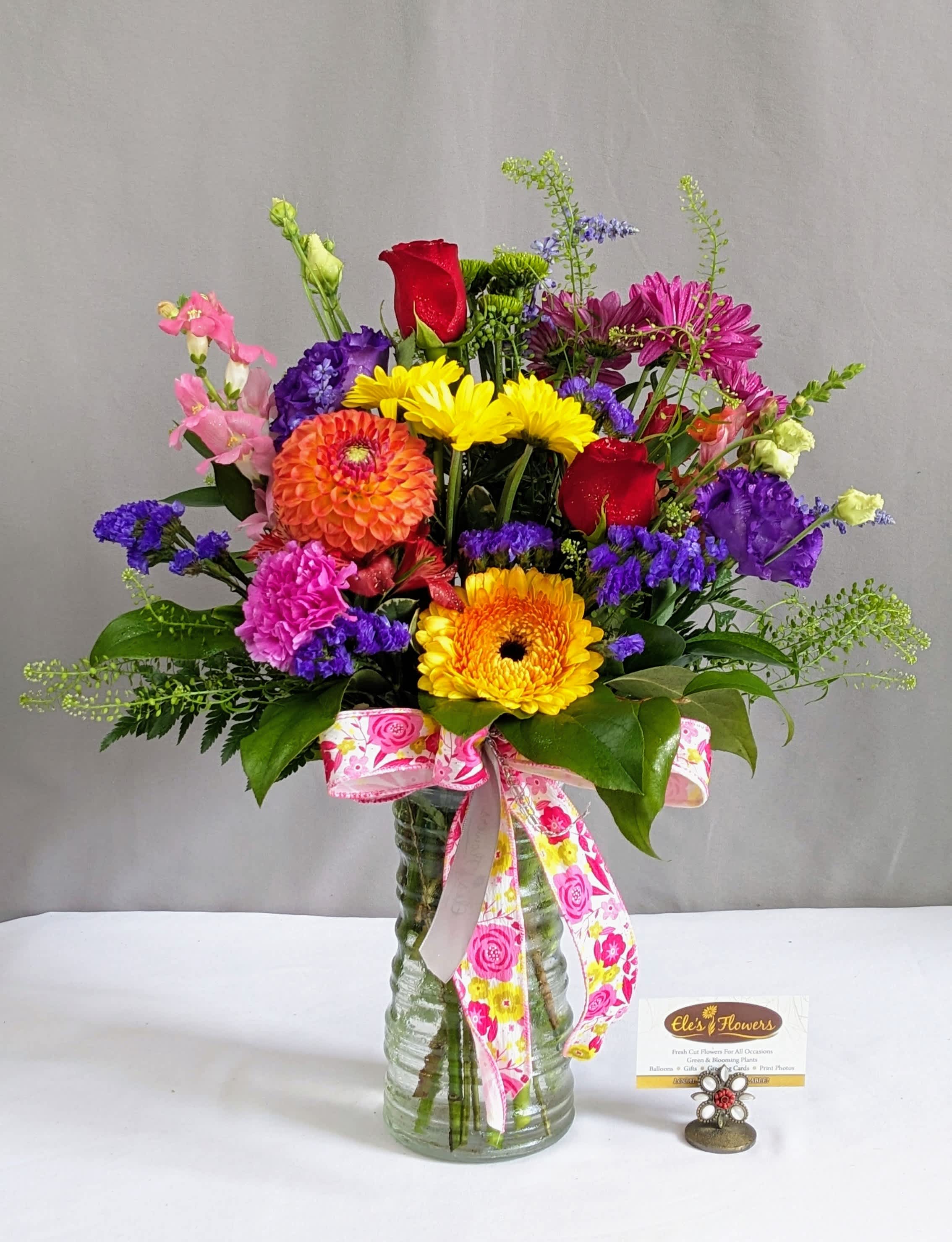 Colorful mixed bouquet in a glass vase with a pink ribbon