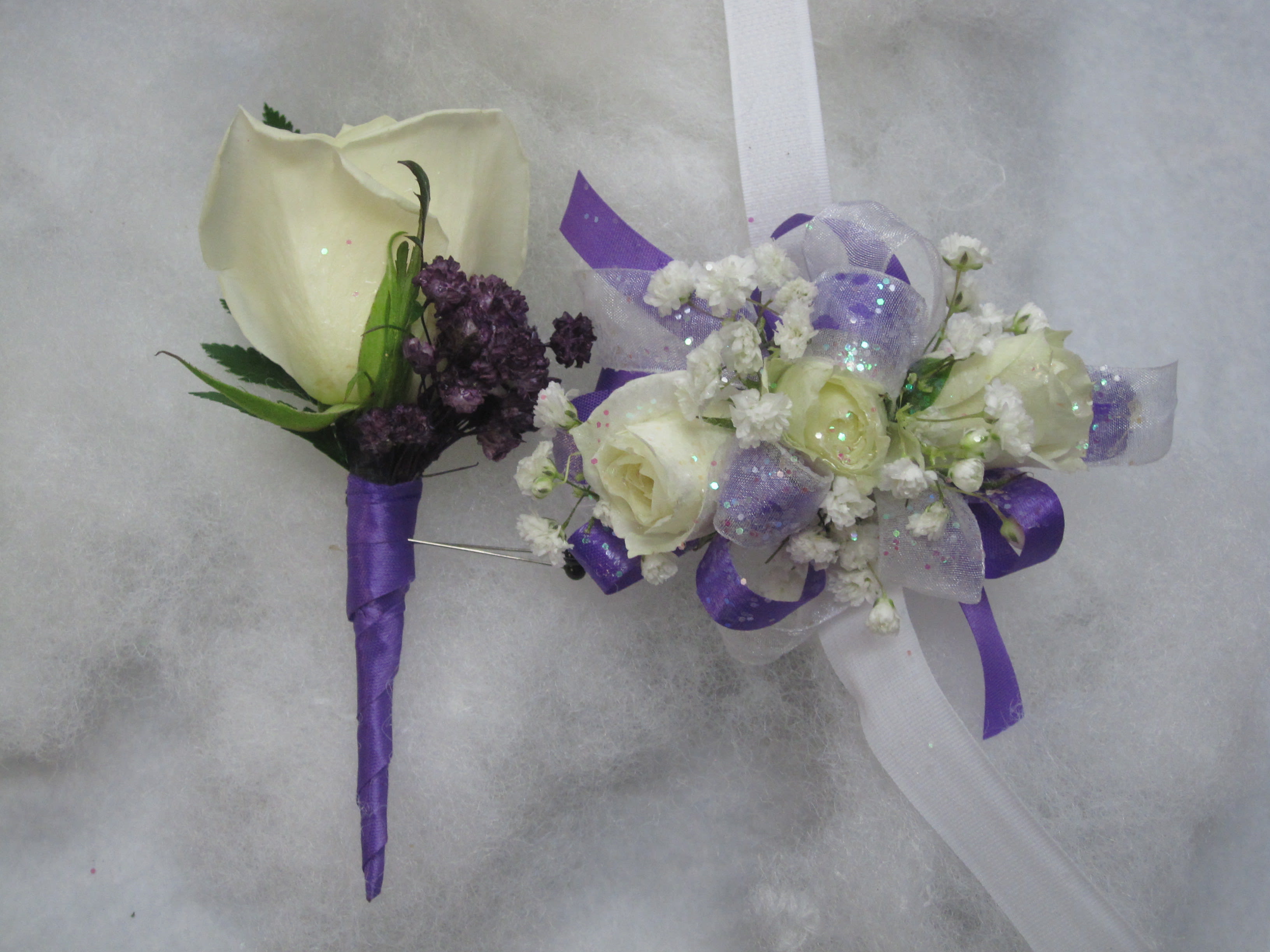 Two floral boutonnieres with white roses and purple accents
