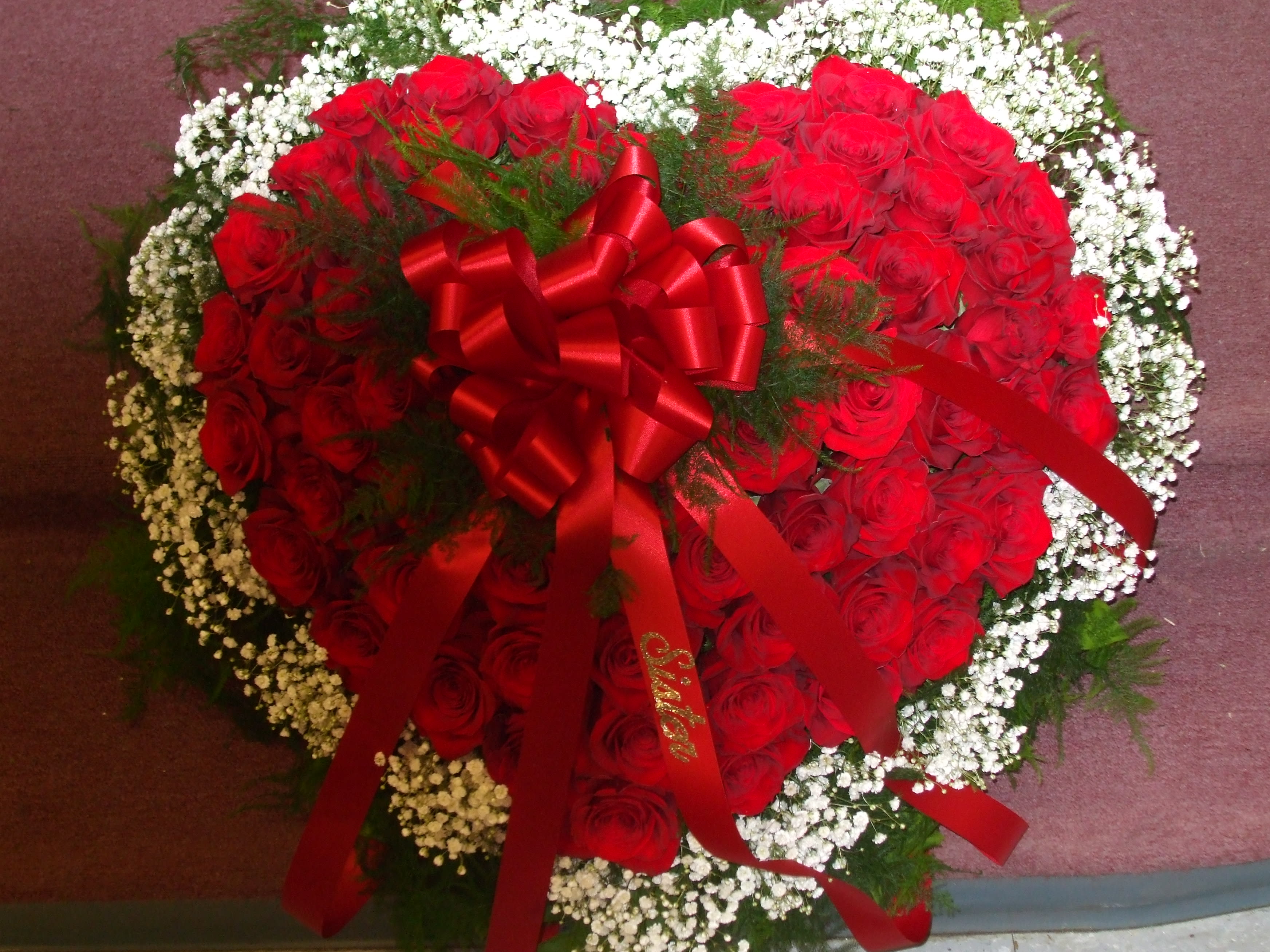 Heart-shaped arrangement of red roses with white baby's breath and a red ribbon bow