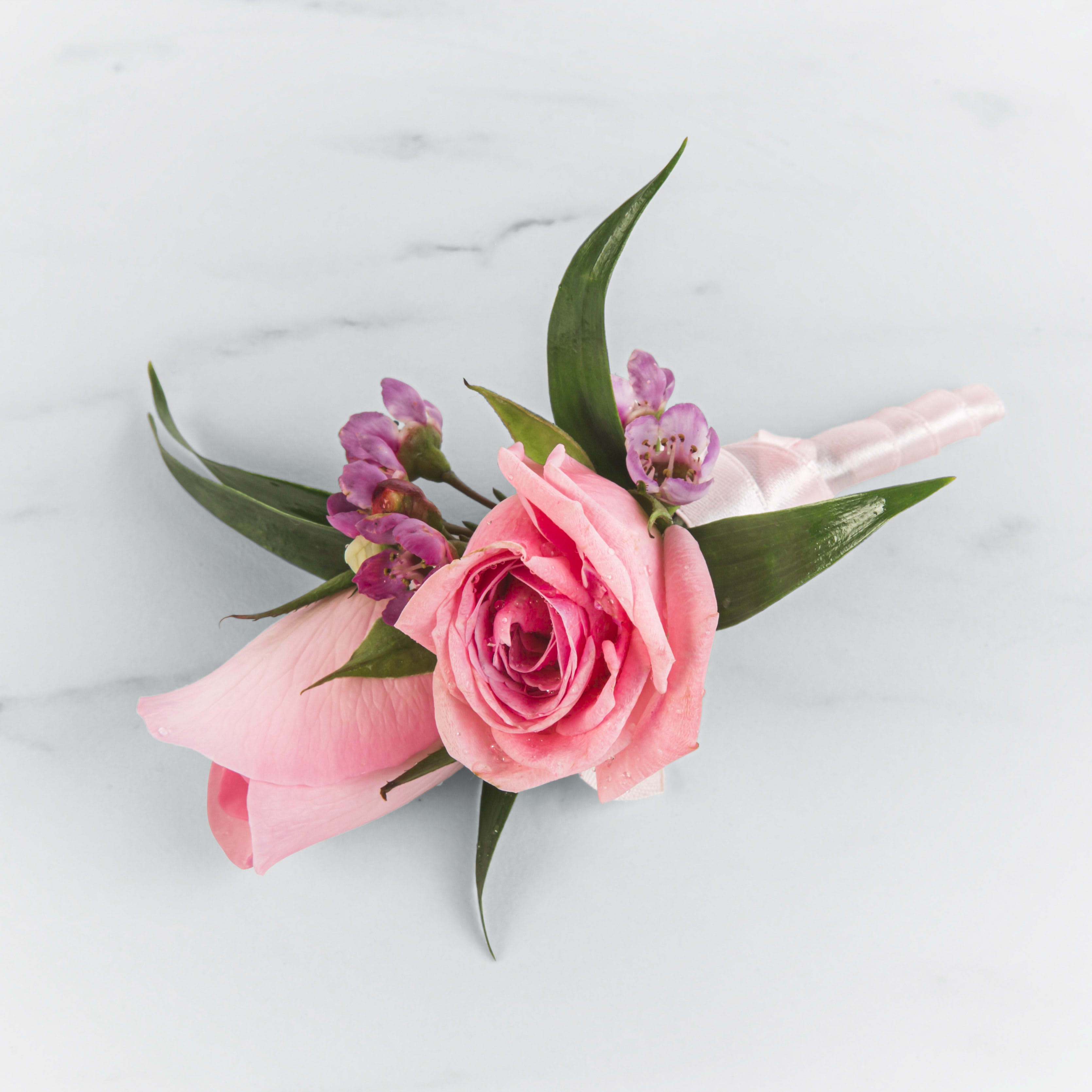 Pink rose boutonniere with small purple accent flowers wrapped in white satin ribbon