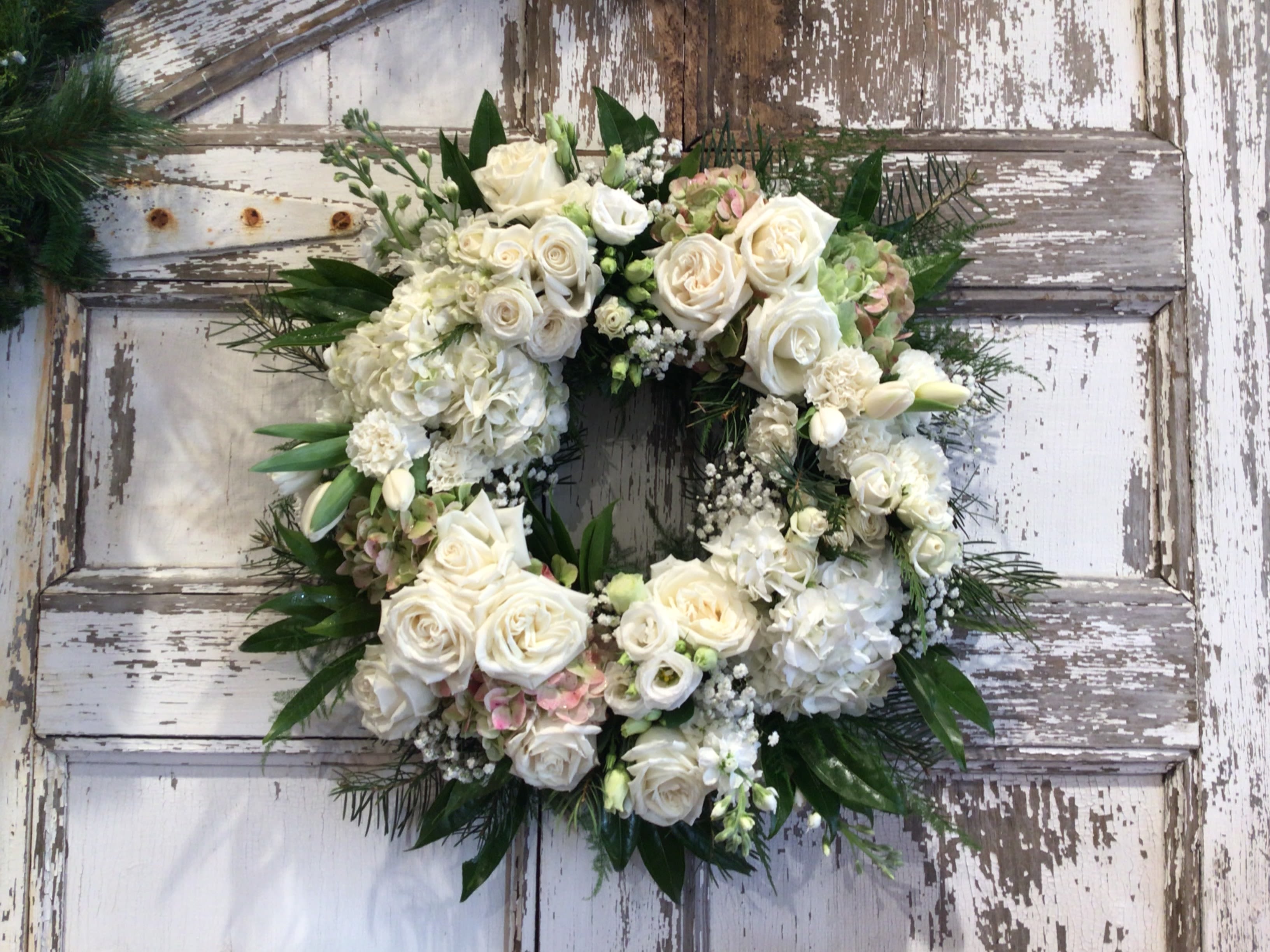 White floral wreath with roses and hydrangeas on a rustic door