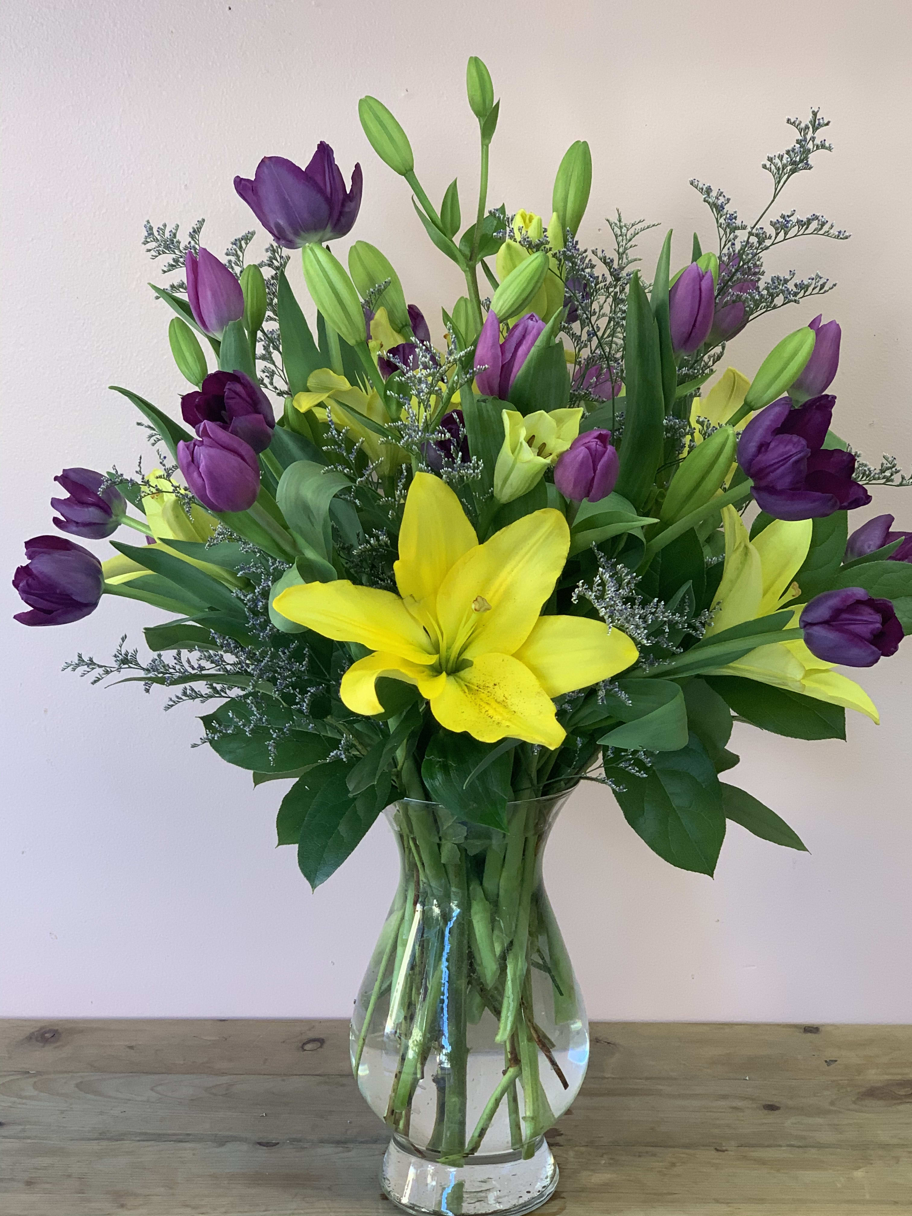 Bouquet of yellow lilies and purple tulips in a clear glass vase