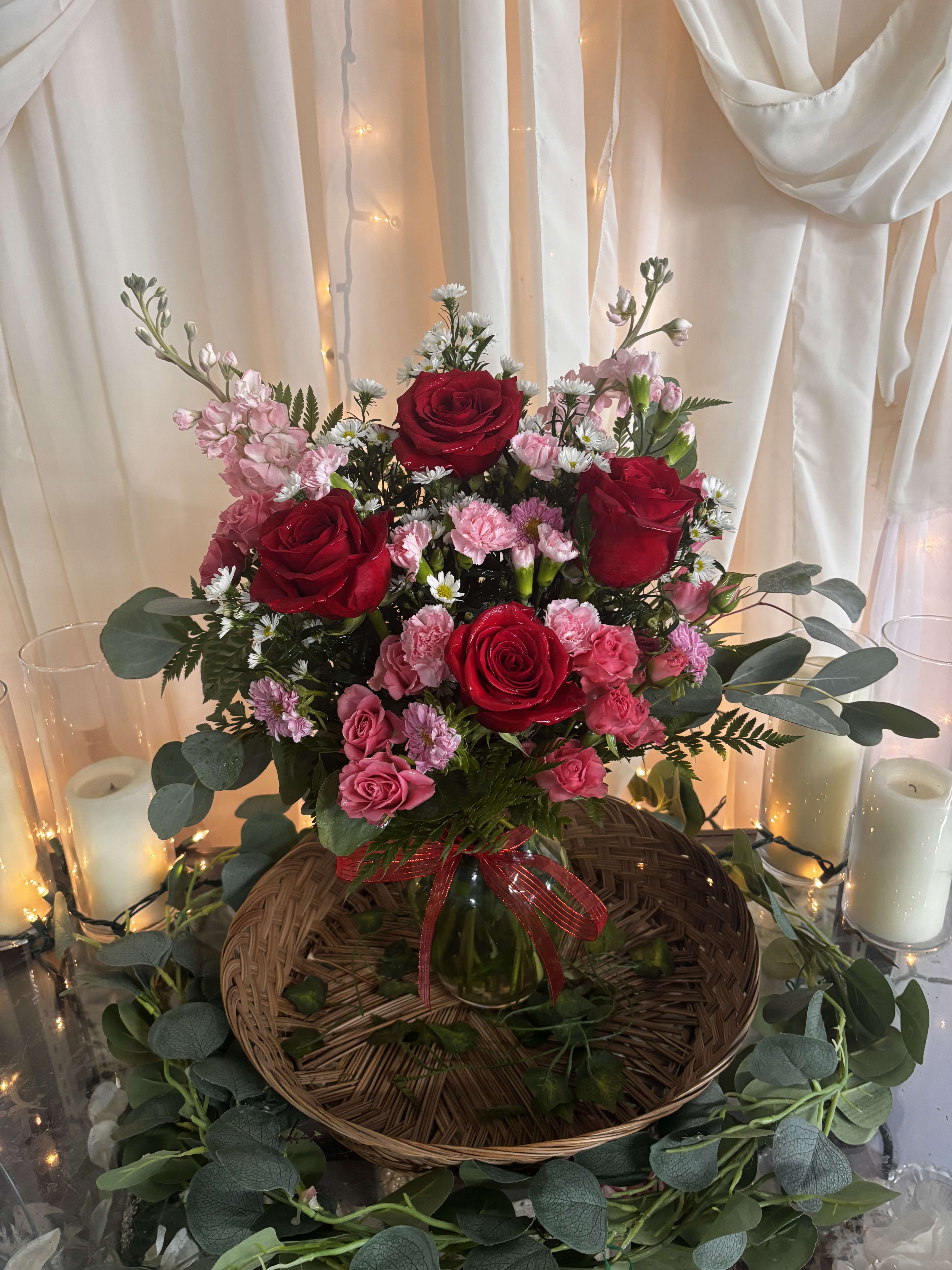 Red and pink rose arrangement in a glass vase with candles and draped fabric