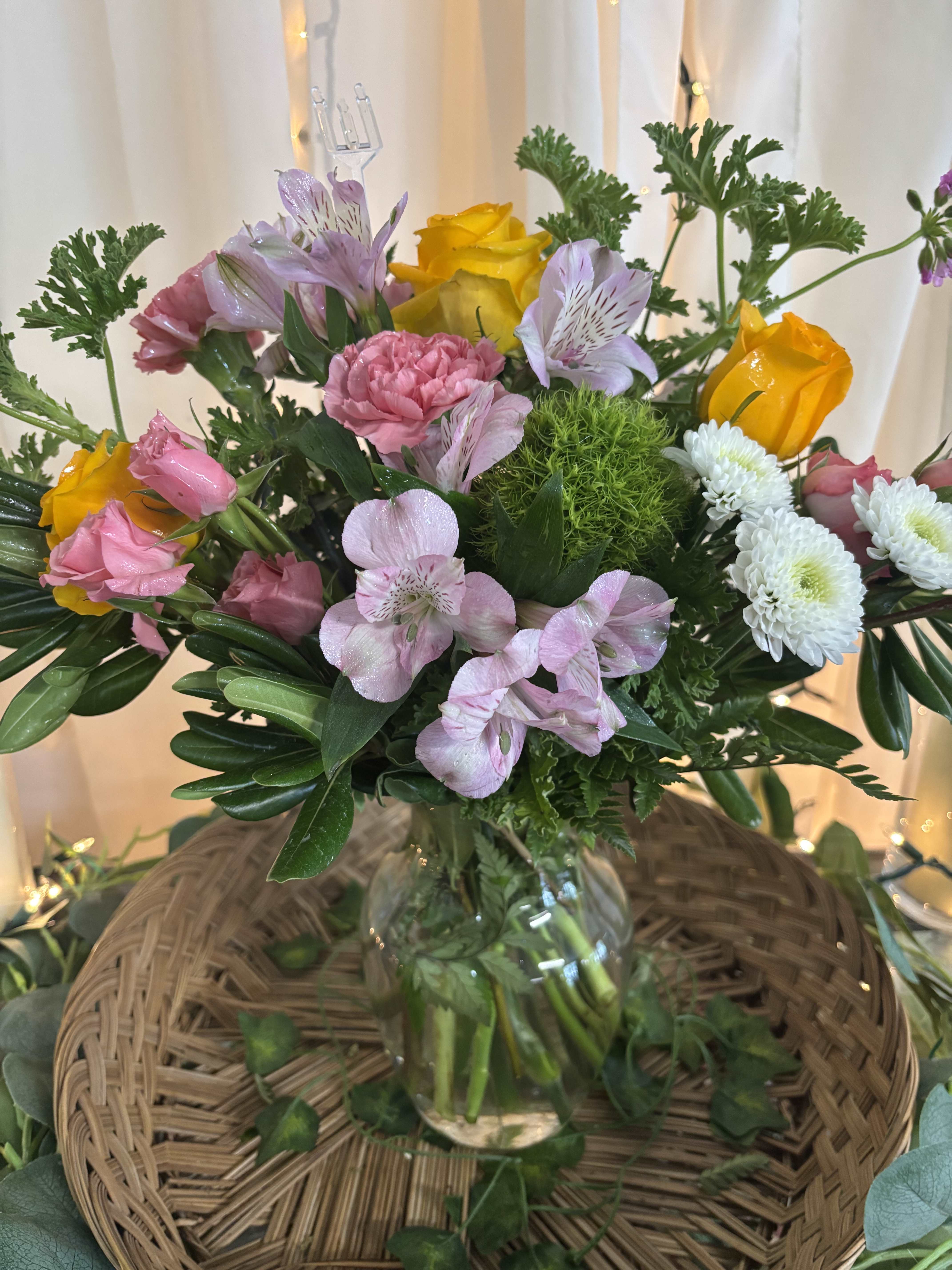 Mixed bouquet of pink, yellow, and white flowers in a glass vase