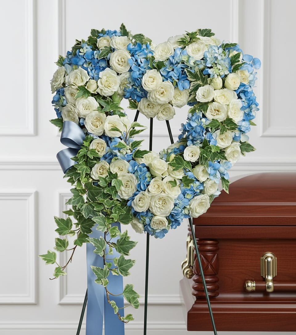 Heart-shaped floral wreath with white roses and blue hydrangeas on a stand