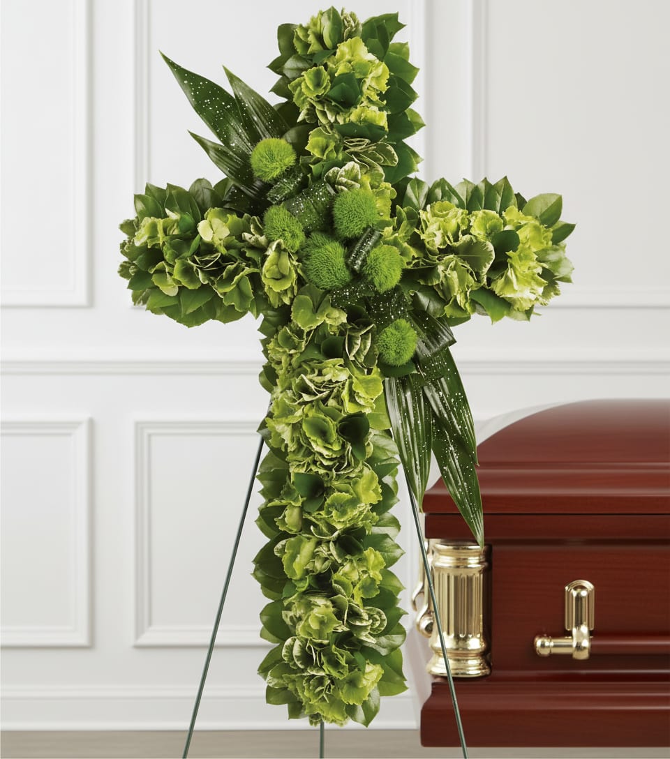 Green floral cross on a stand beside a casket