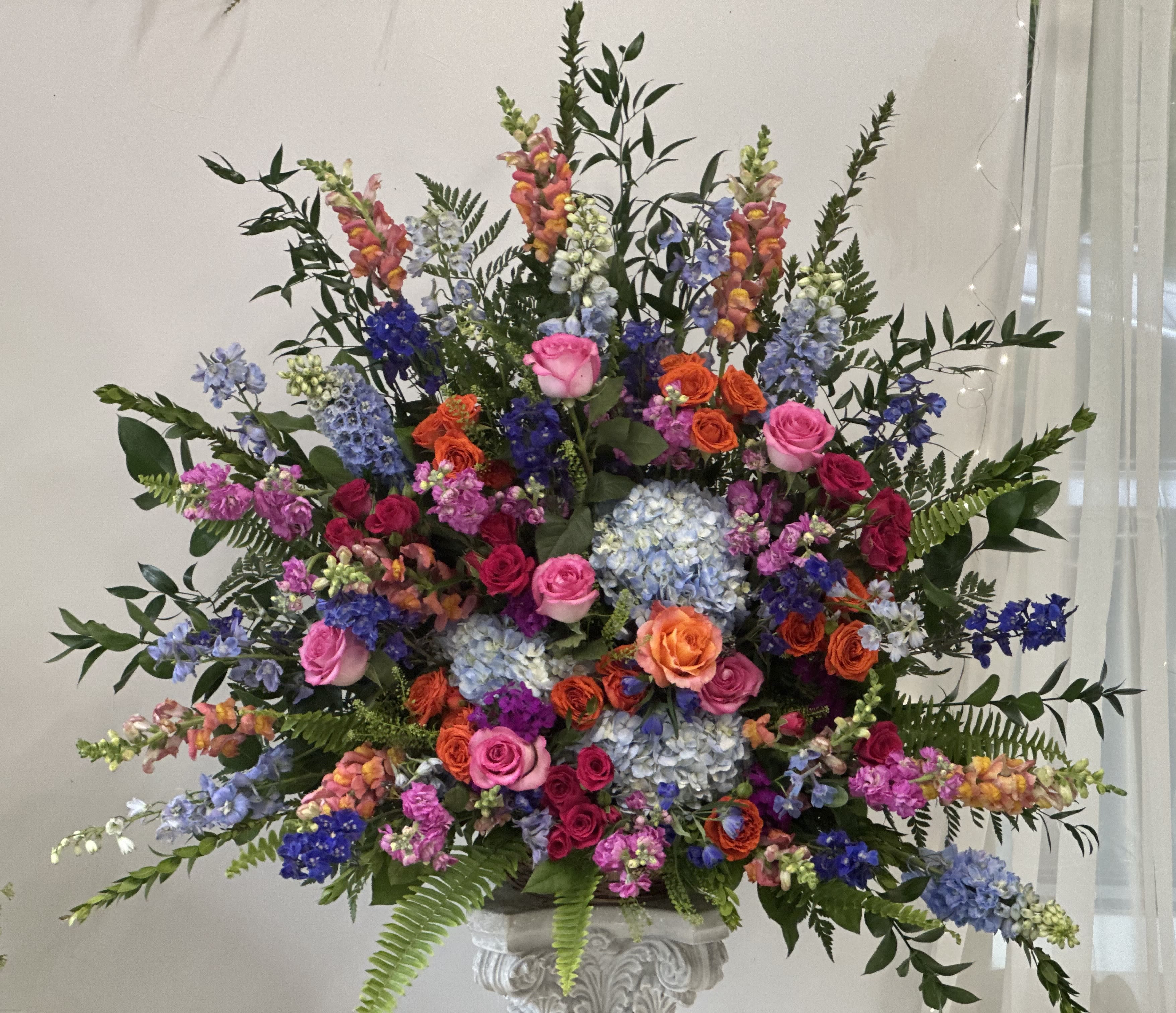 Large mixed floral arrangement with roses, hydrangeas, and snapdragons in a pedestal vase