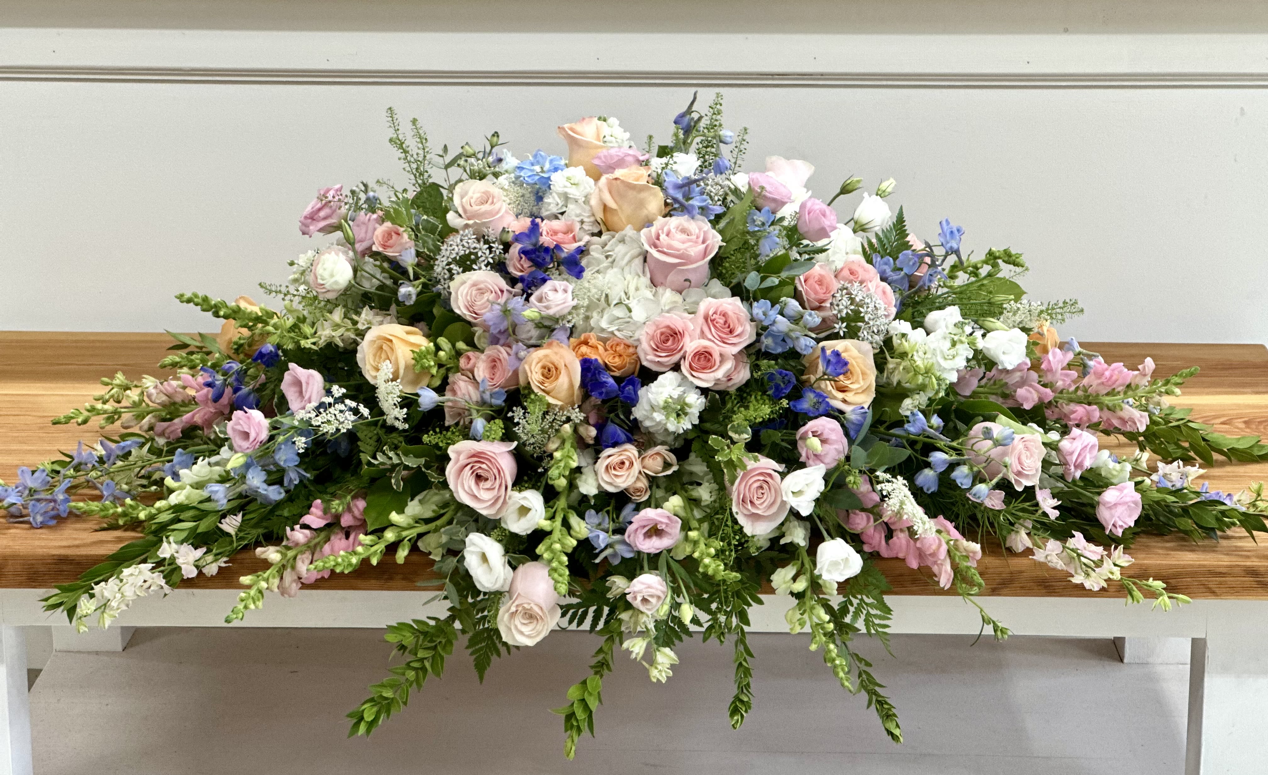 Large pastel floral casket spray with roses and blue blooms