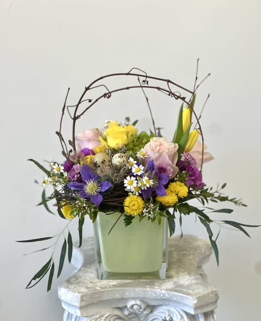 Pastel Easter Arrangement by Westford Florist Art by Veny - Elevate your Easter celebrations with the Pastel Easter Arrangement by Westford Florist Art by Veny. This exquisite floral masterpiece combines delicate pink roses, bright yellow tulips, and a charming assortment of blooms including spray roses, clematis, chamomile, carnations, hydrangea, and vibrant button poms in yellow and purple hues. Each arrangement is thoughtfully accented with natural grapevine elements and real quail egg shells, creating an enchanting centerpiece that captures the essence of spring. Perfect for gatherings or as a heartfelt gift, this stunning display brings warmth and beauty to any setting while showcasing the artistry of skilled floristry. Celebrate renewal and joy with this captivating seasonal arrangement,