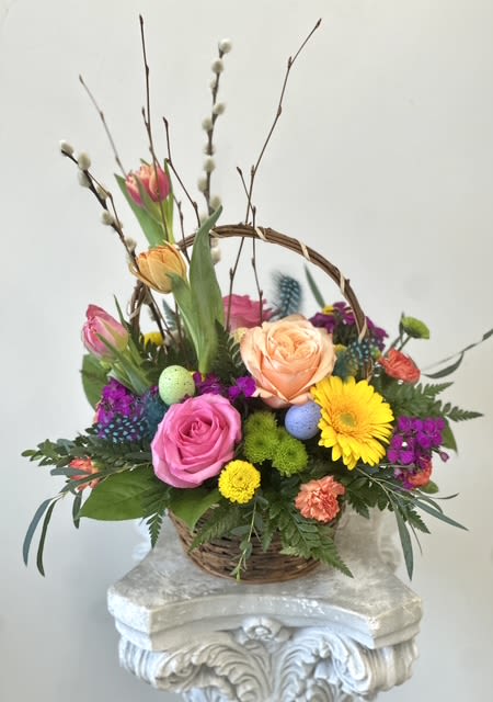 Easter Blooms Basket by Westford Florist Art by Veny - Elevate your Easter celebration with the exquisite Easter Blooms Basket by Westford Florist Art by Veny. This artistically arranged basket features a harmonious blend of peach and pink roses, vibrant tulips, cheerful yellow gerberas, delicate sweet william, and charming purple button poms. Beautifully accented with lush pussy willow, spring branches, and whimsical touches of Easter egg shells and feathers, this design embodies the spirit of renewal that comes with spring.Perfect for gifting or adding a touch of elegance to your holiday decor, this stunning floral composition promises to brighten any space while delighting the senses. Celebrate the season in style with a centerpiece that captures both artistry and joy—truly a floral masterpiece for your festive gathering.