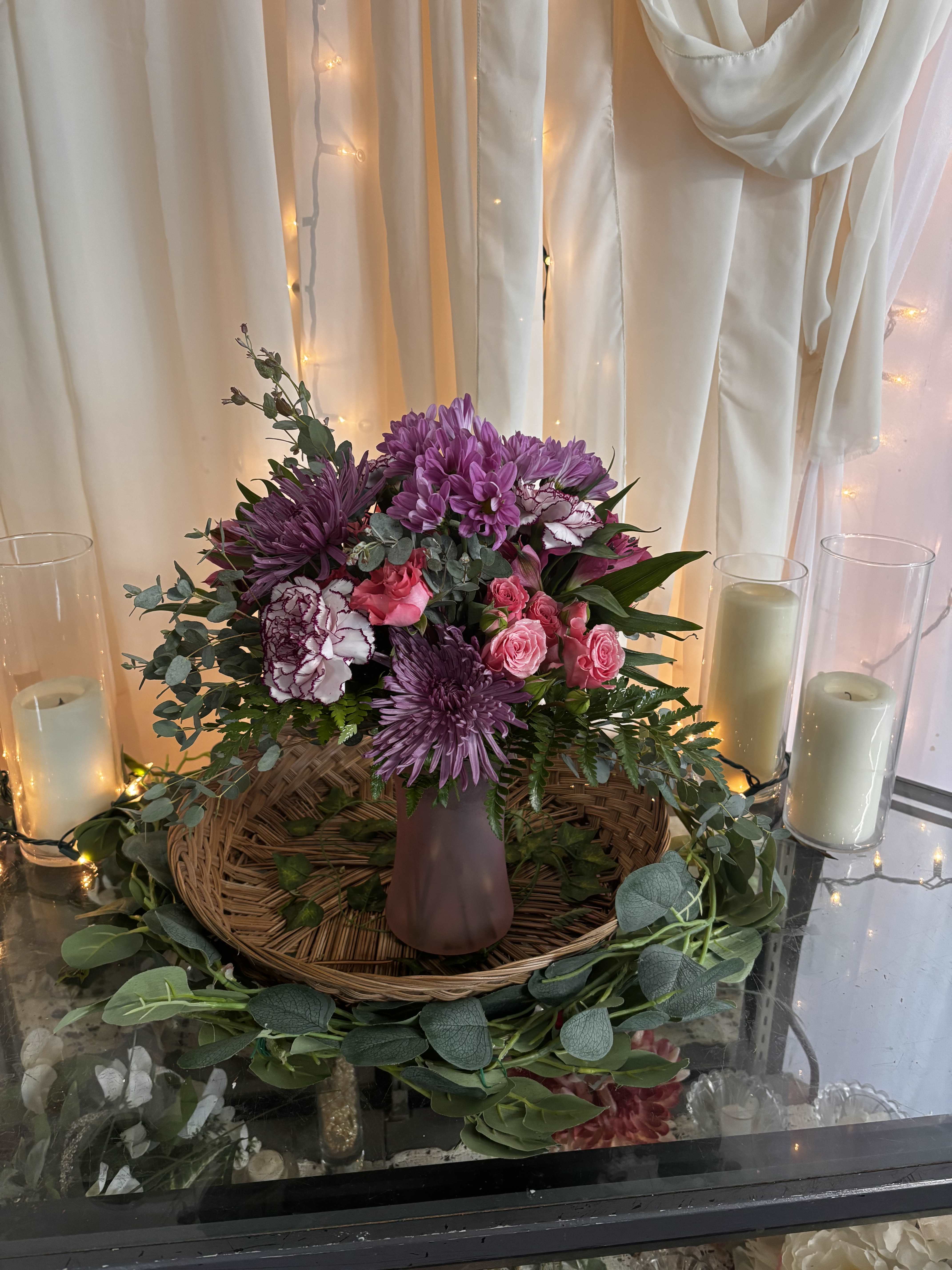 Purple and pink floral arrangement in a mauve vase with candles nearby