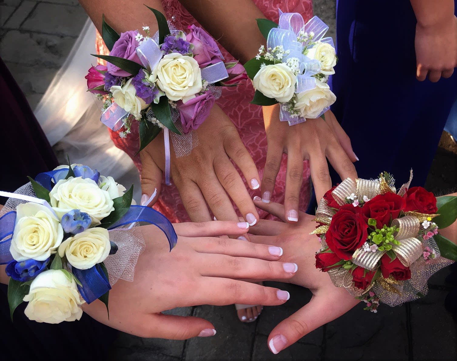 Hands wearing rose corsages in red, white, blue, and lavender