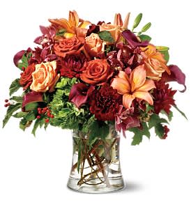 Mixed bouquet of orange, red, and peach flowers in a clear glass vase