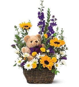 Basket arrangement with a teddy bear surrounded by yellow, white, and purple flowers