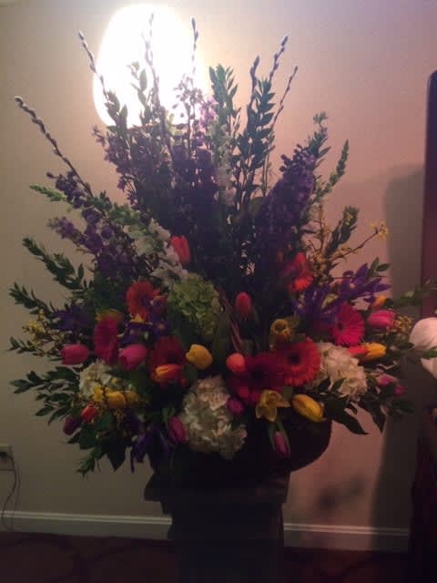 Tall mixed flower arrangement with bright tulips and gerbera daisies in a dark vase