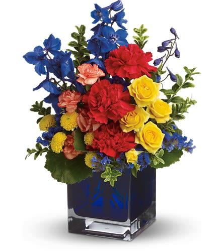 Bright mixed bouquet in a square glass vase with blue, red, and yellow flowers