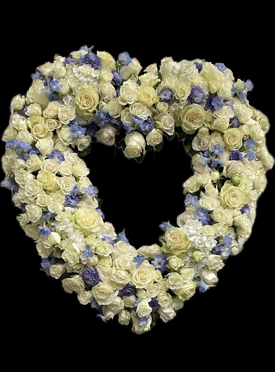 Heart-shaped floral arrangement of white roses and blue flowers