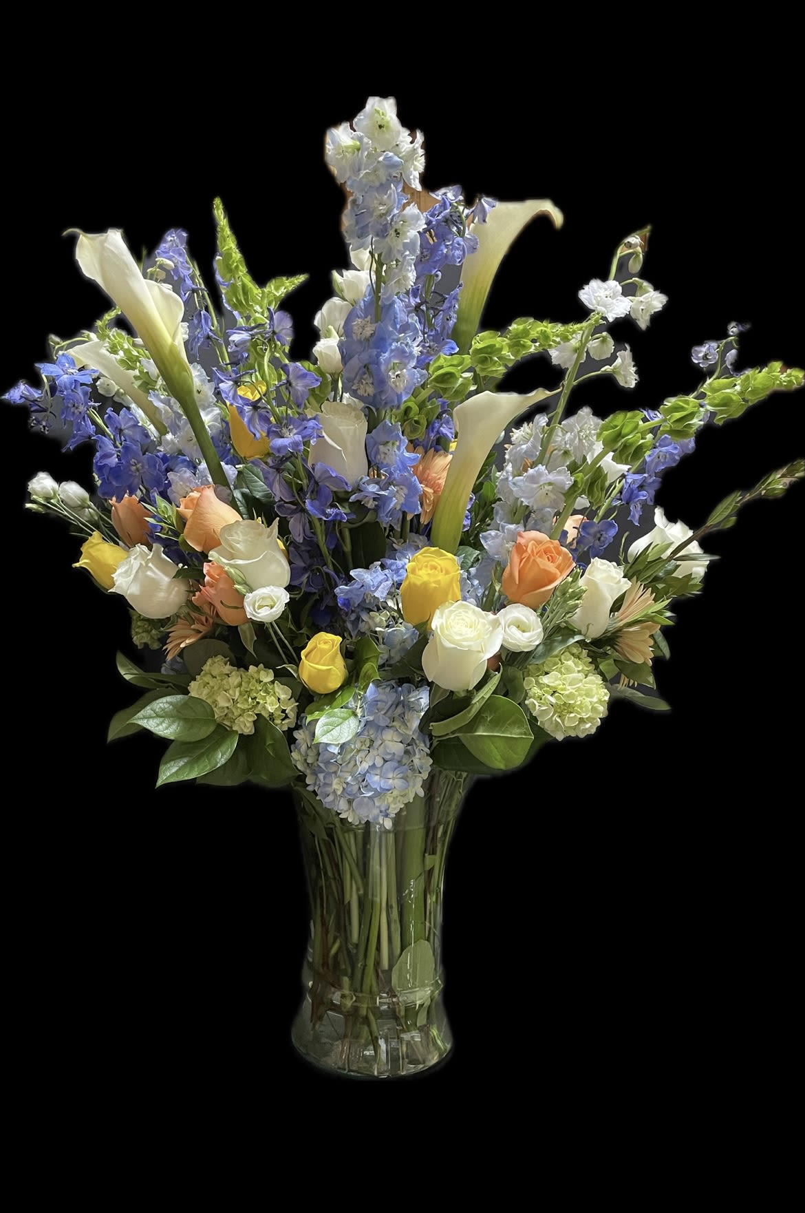Tall mixed bouquet of blue and white flowers in a clear glass vase