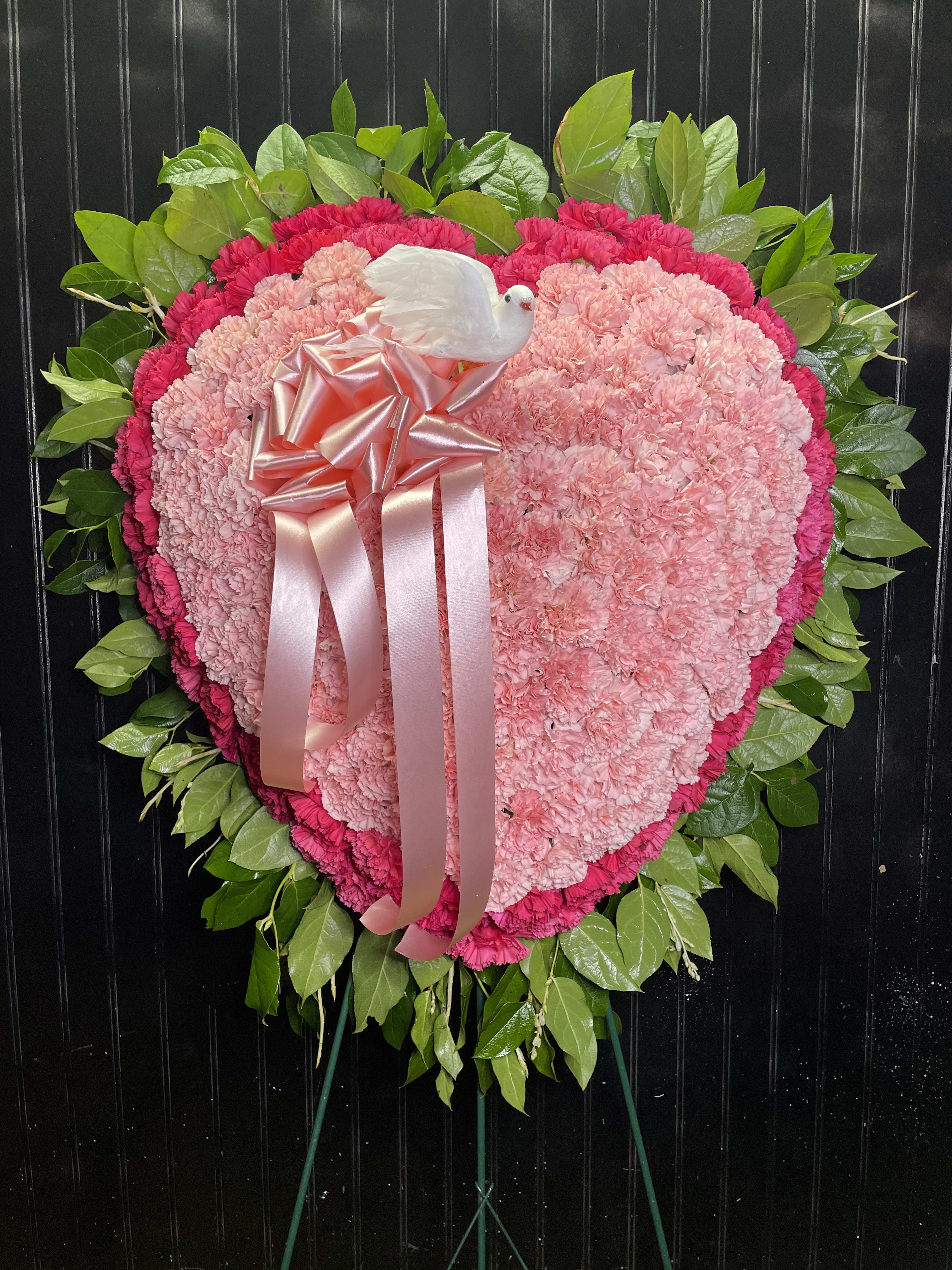 Heart-shaped pink carnation wreath with a ribbon and white dove