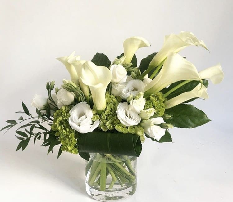 White calla lilies and white blooms arranged in a clear glass vase