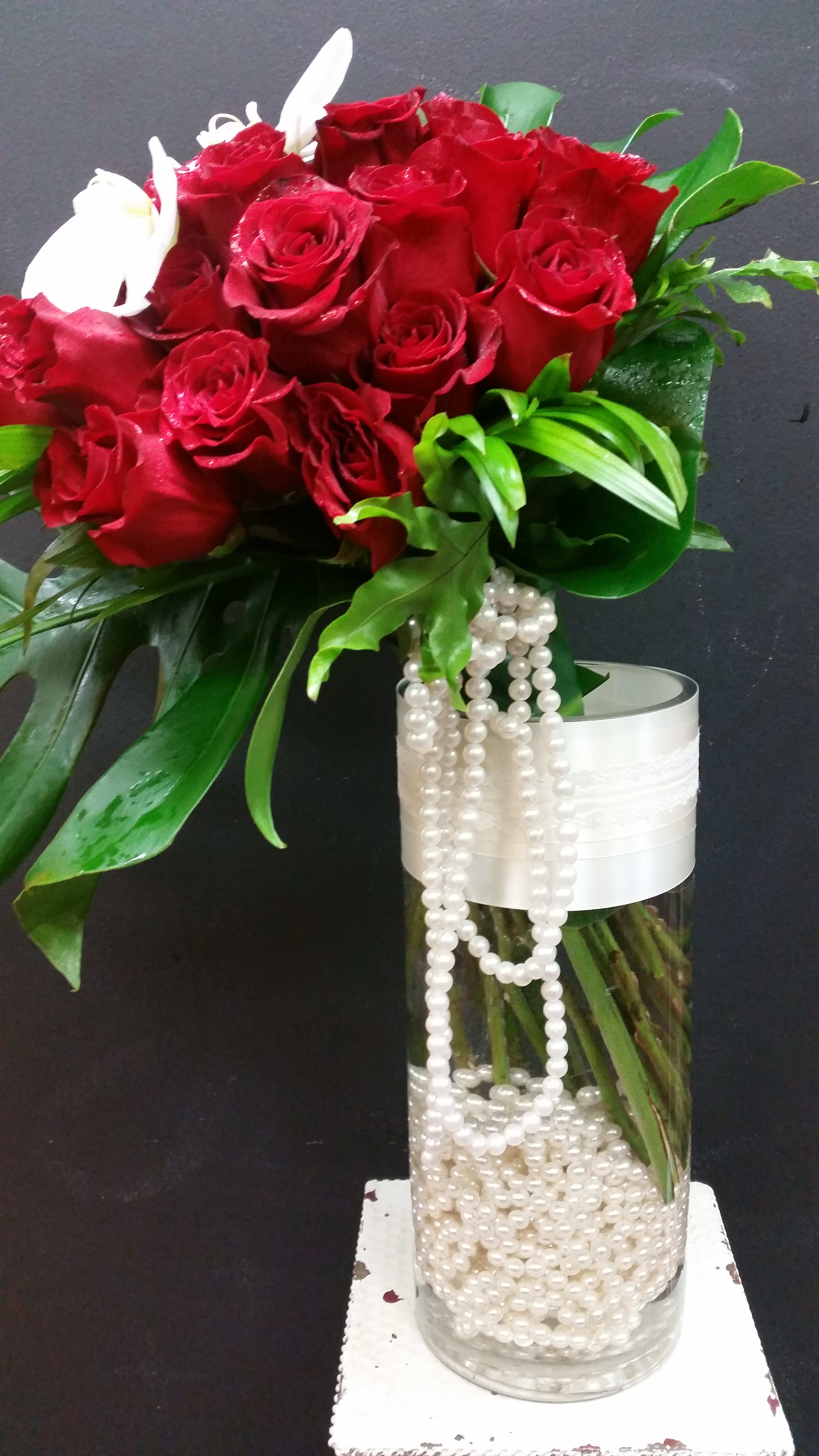 Red roses in a tall glass vase with white bead strands