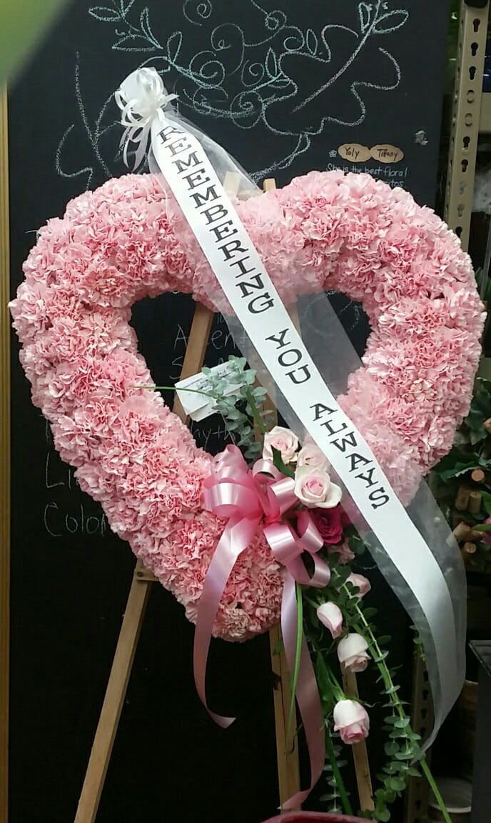 Pink heart-shaped floral wreath with a memorial ribbon on an easel