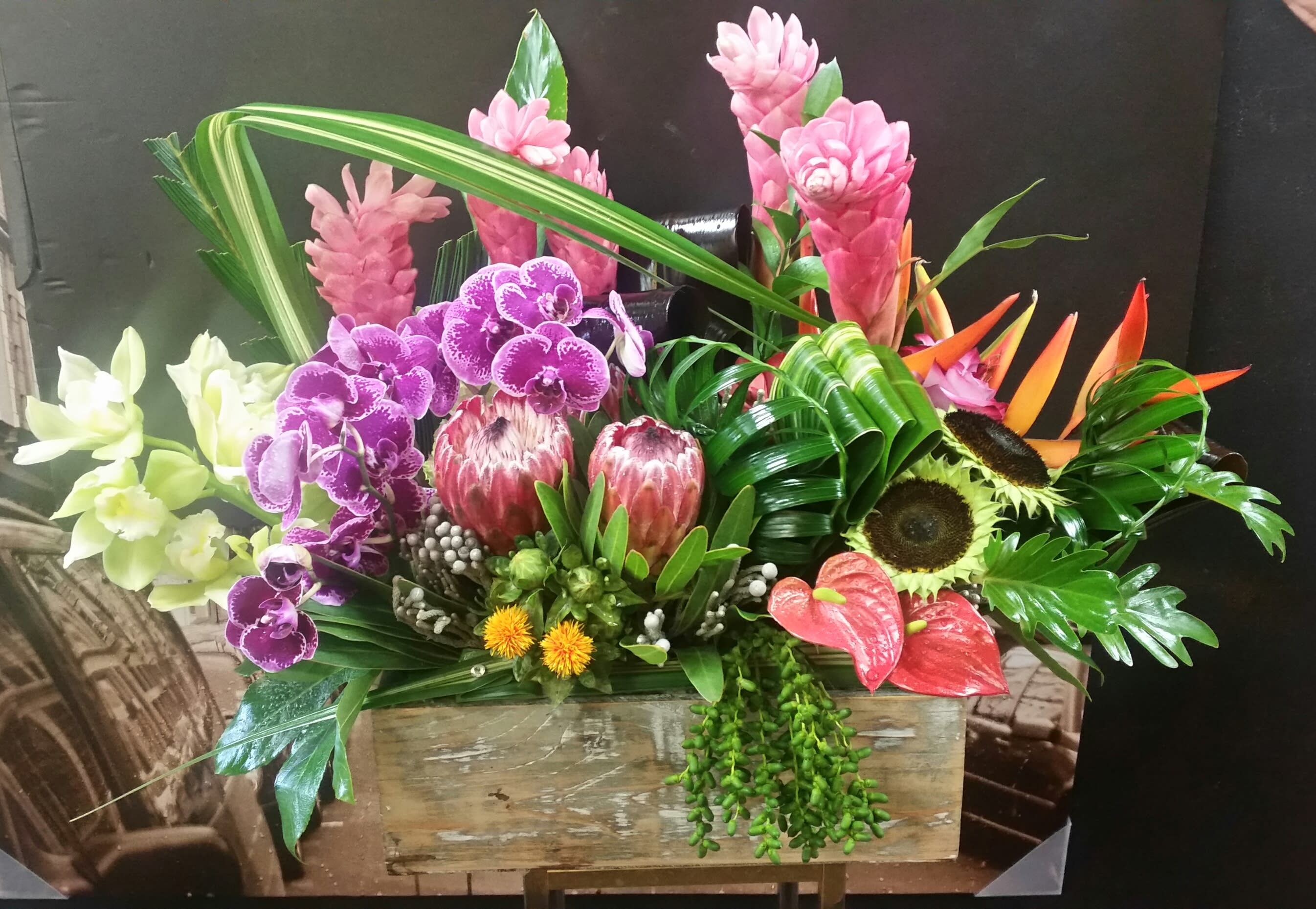 Tropical floral arrangement with orchids, protea, and bird of paradise in a wooden box