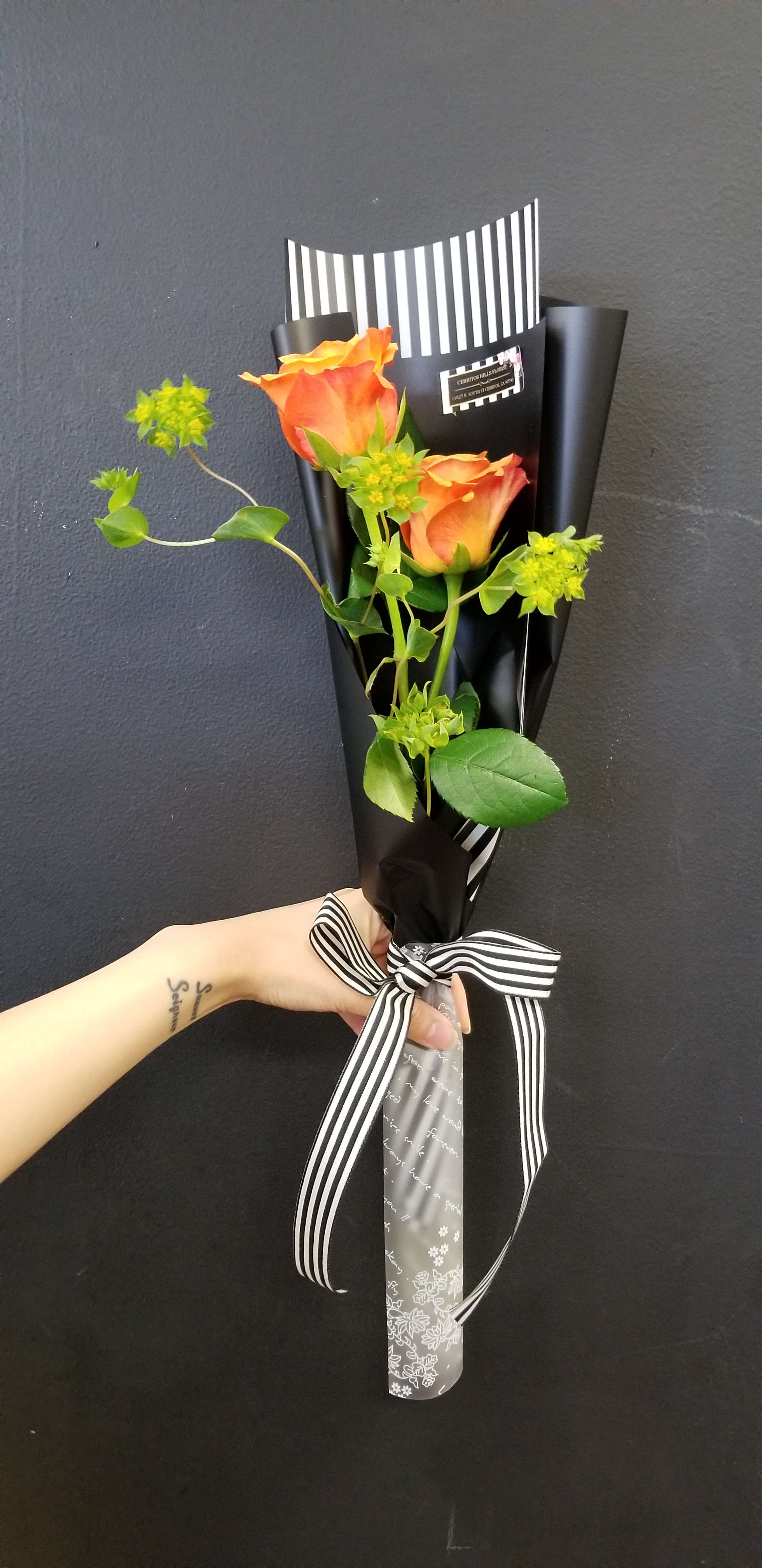 Two orange roses wrapped in black paper with a striped ribbon
