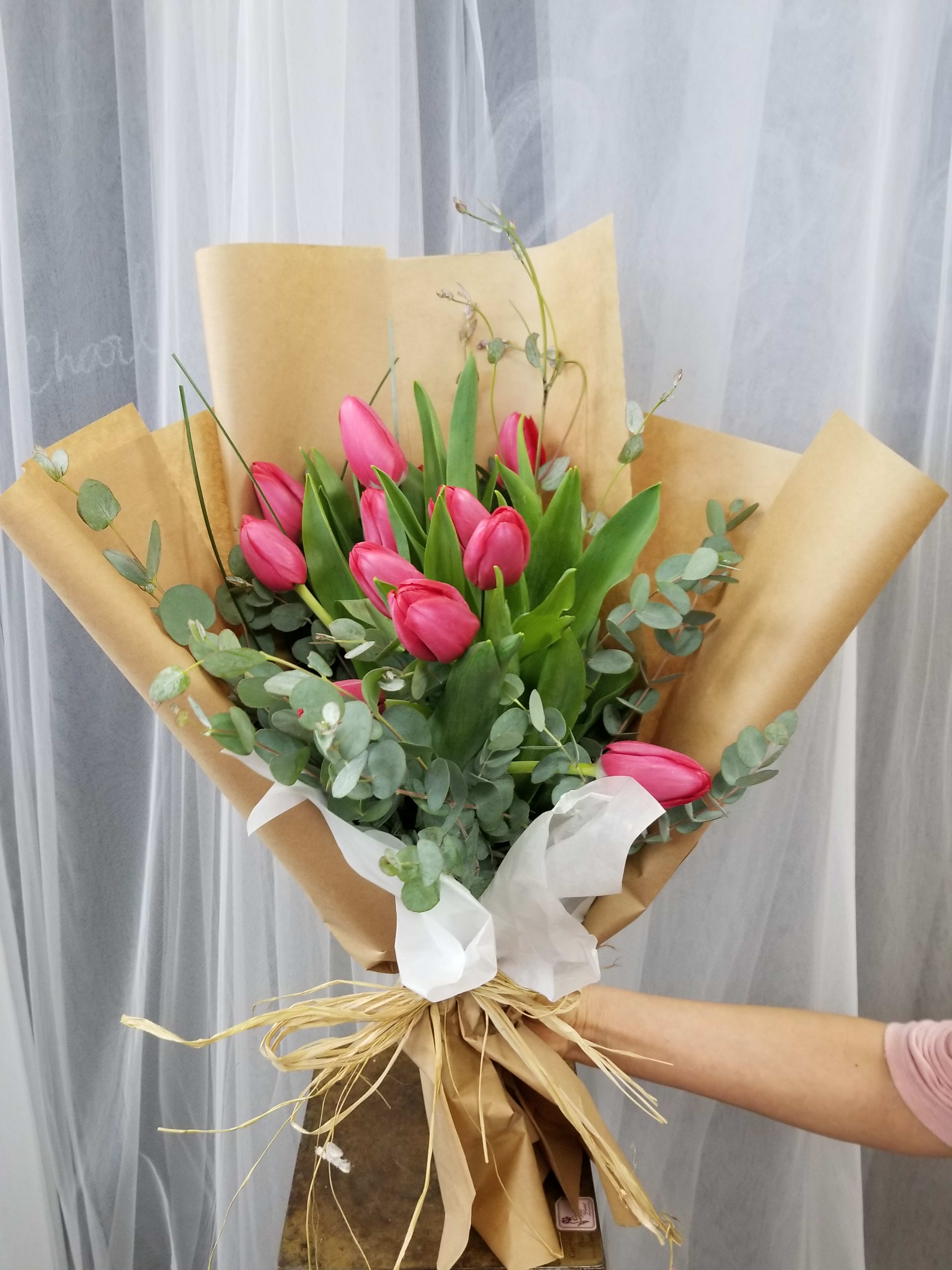 Pink tulip bouquet wrapped in brown paper with white ribbon
