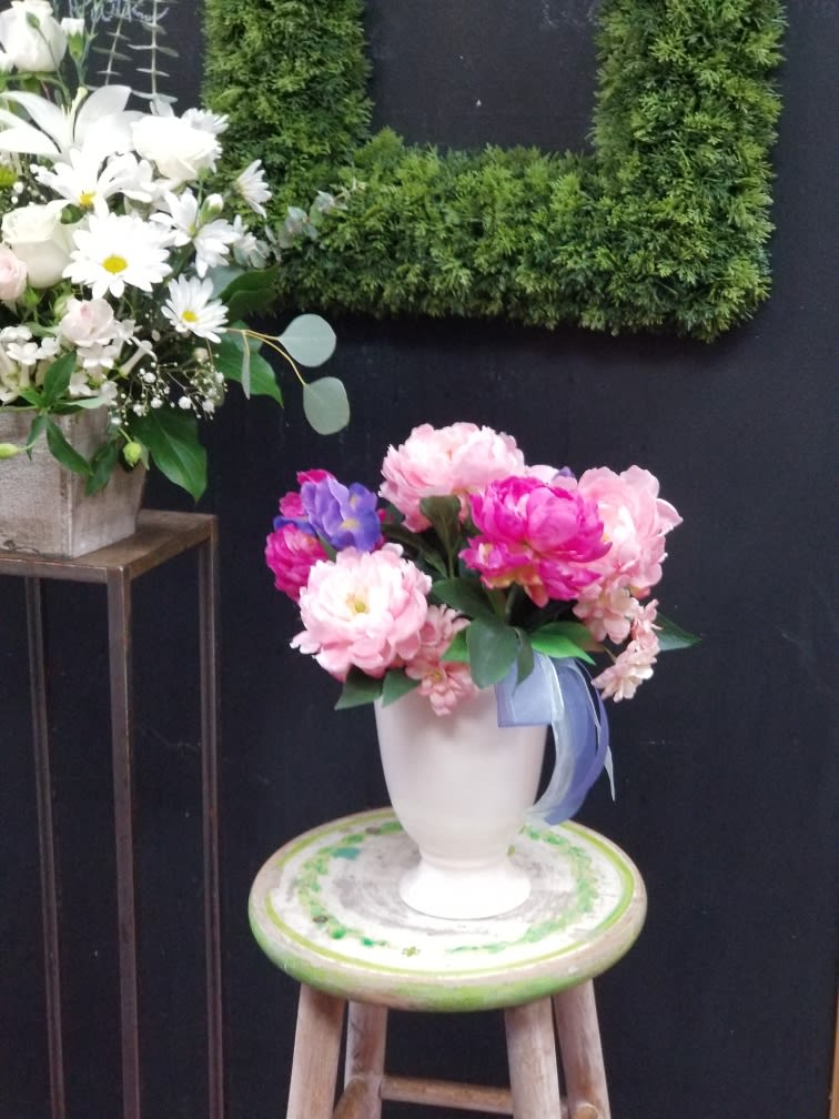 Pink and purple flowers arranged in a white vase on a stool