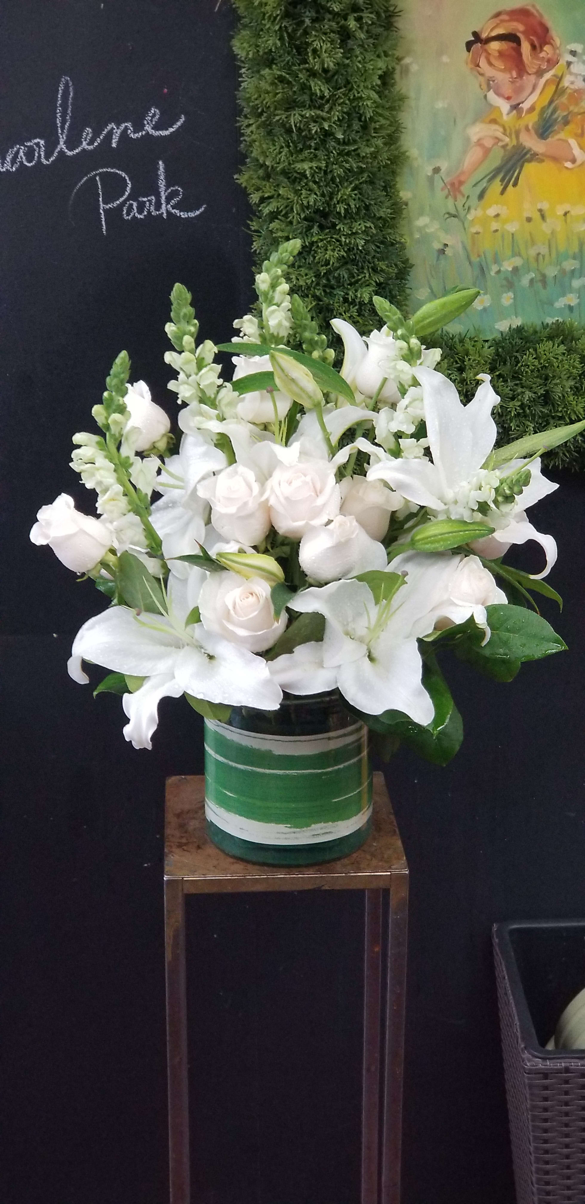 White lilies and pale roses arranged in a green glass vase