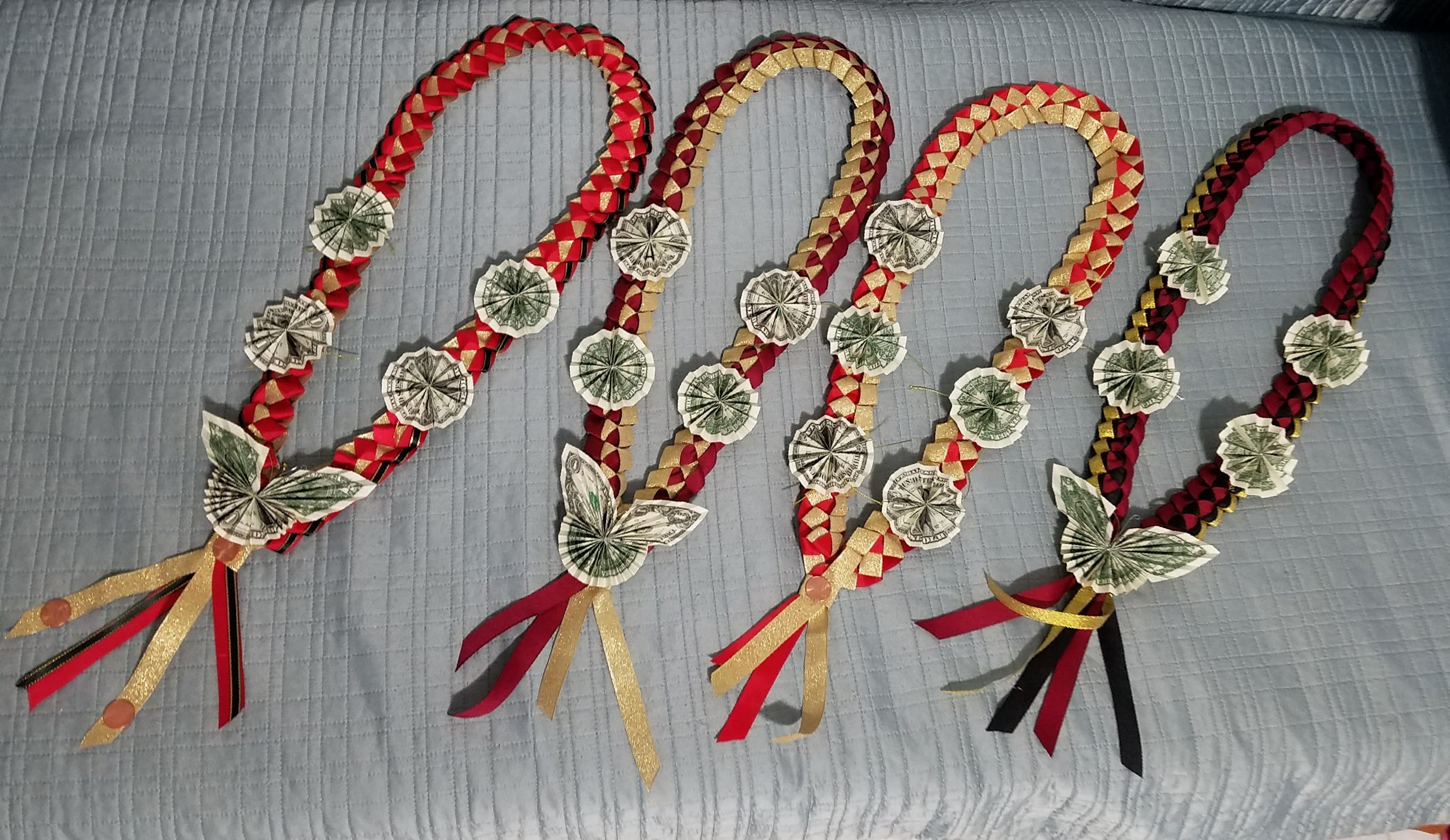 Four braided money garlands with ribbon tassels laid on a bed