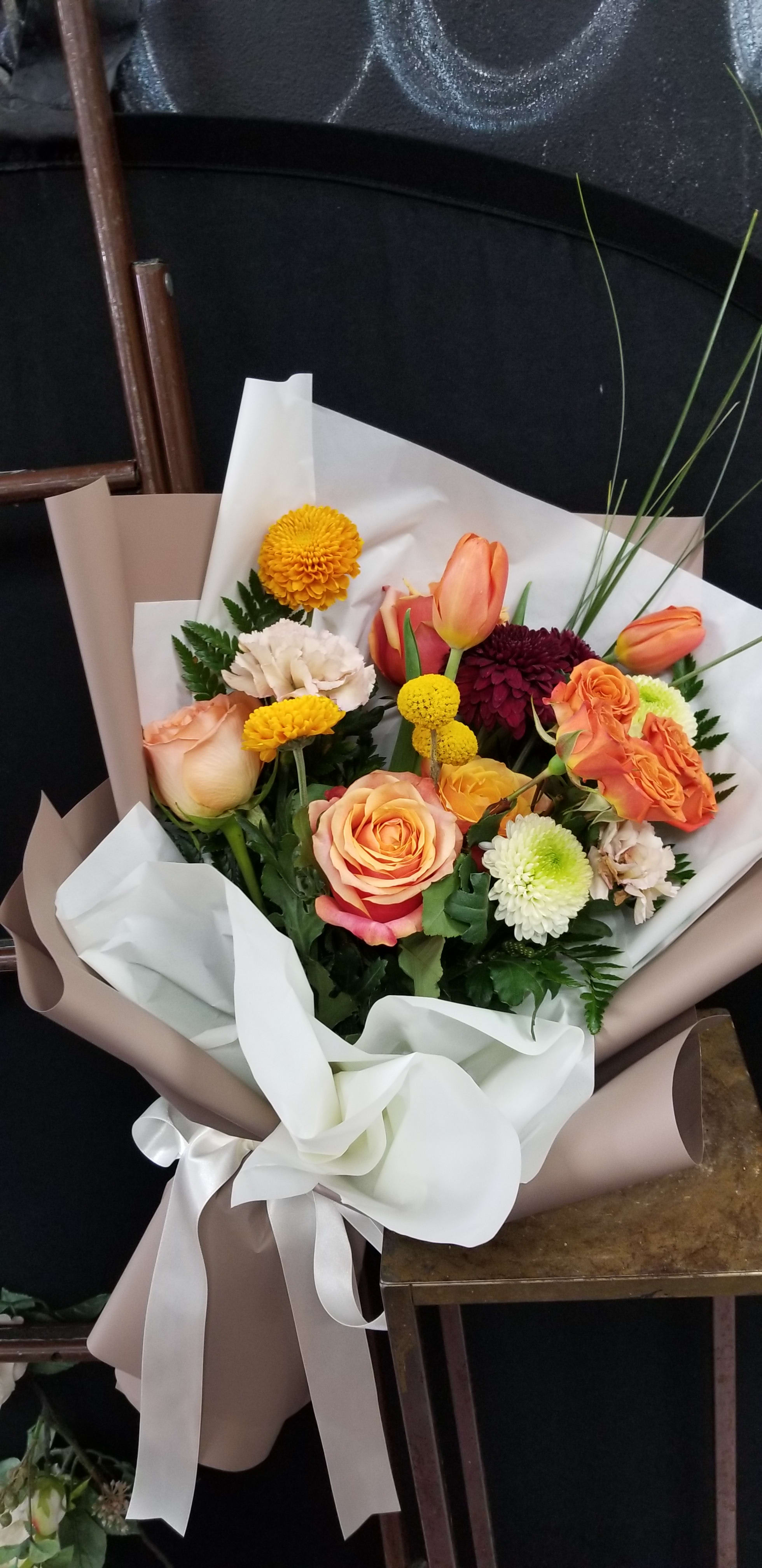 Bouquet of orange and peach roses with mixed chrysanthemums wrapped in white and taupe paper