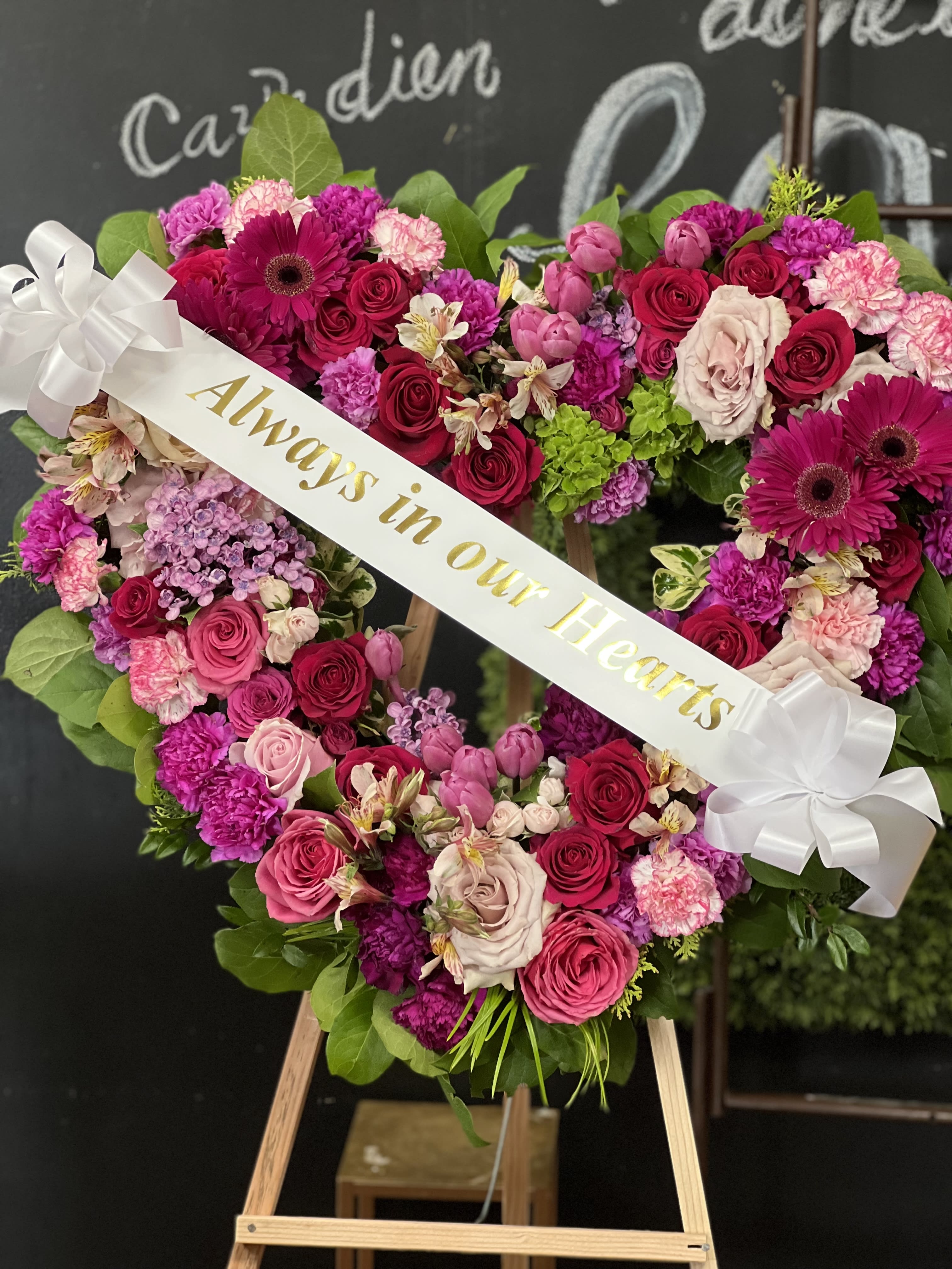 Heart-shaped floral wreath with pink and red roses and a white ribbon