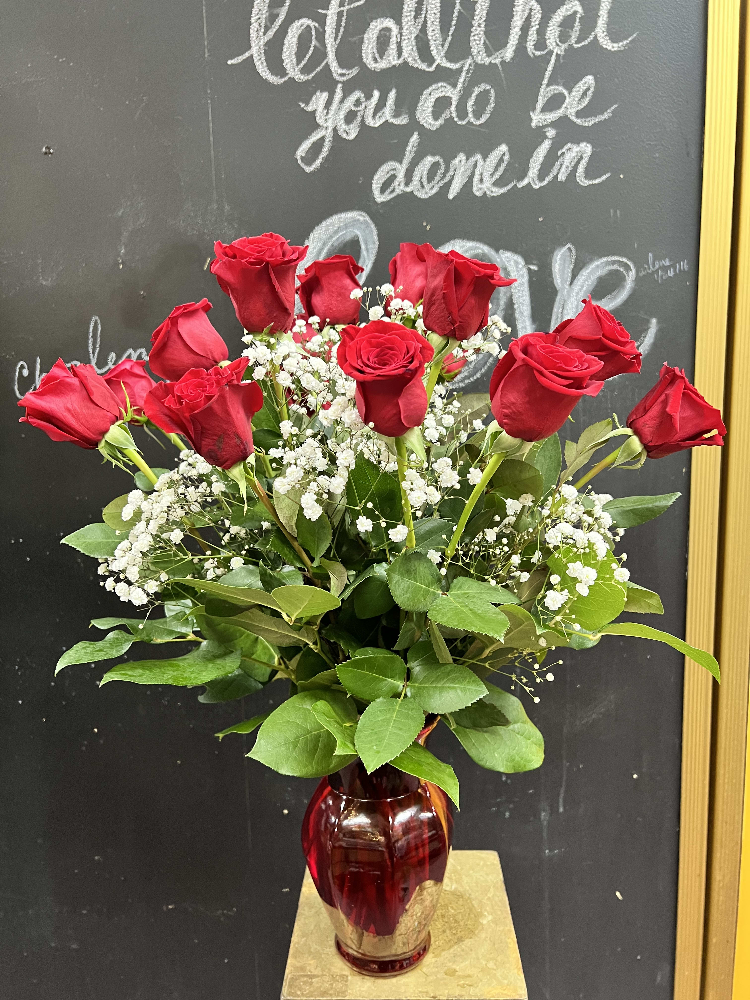 Red roses arranged in a red glass vase with white baby's breath