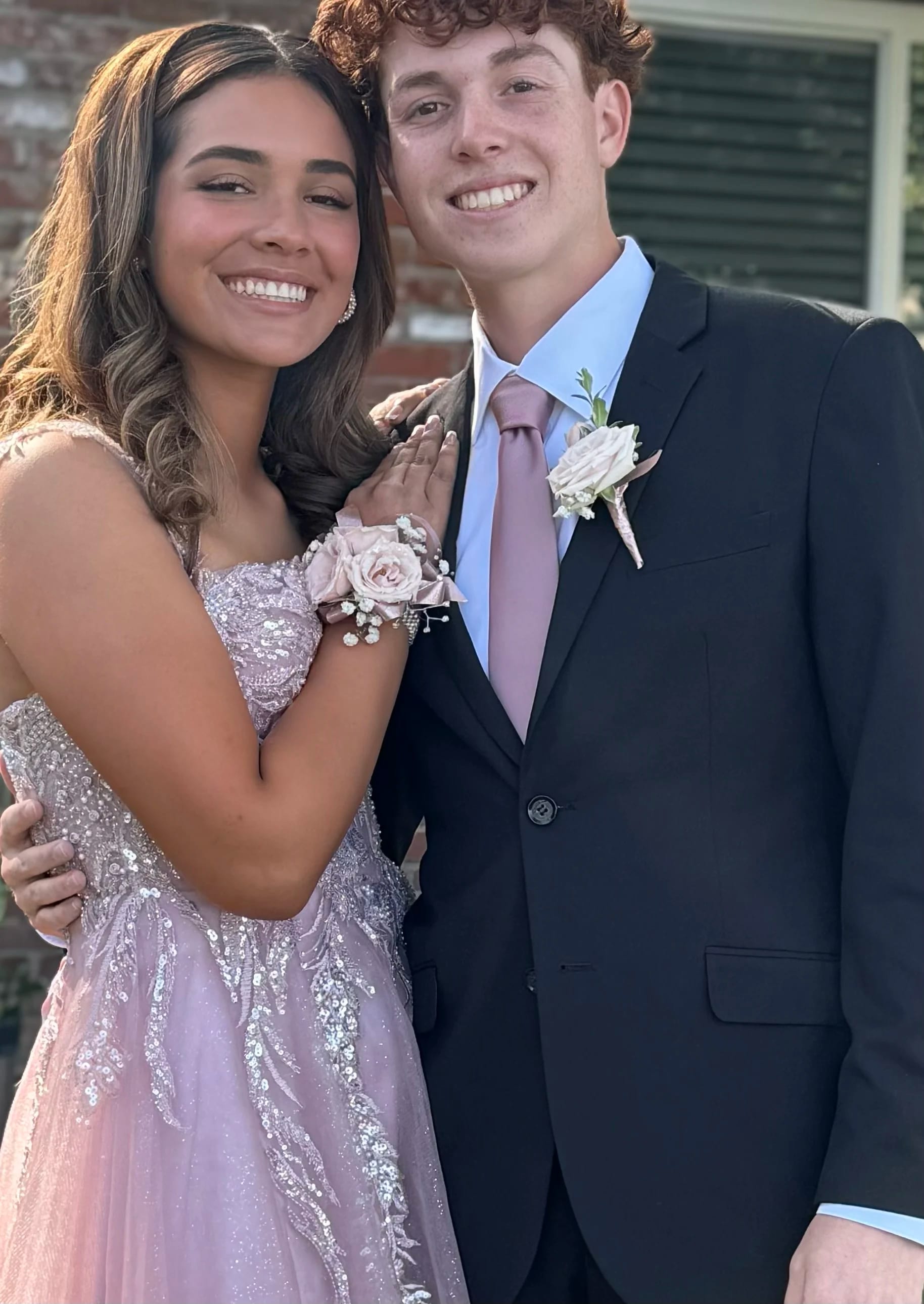 Couple in formal attire wearing matching blush rose wrist corsage and boutonniere