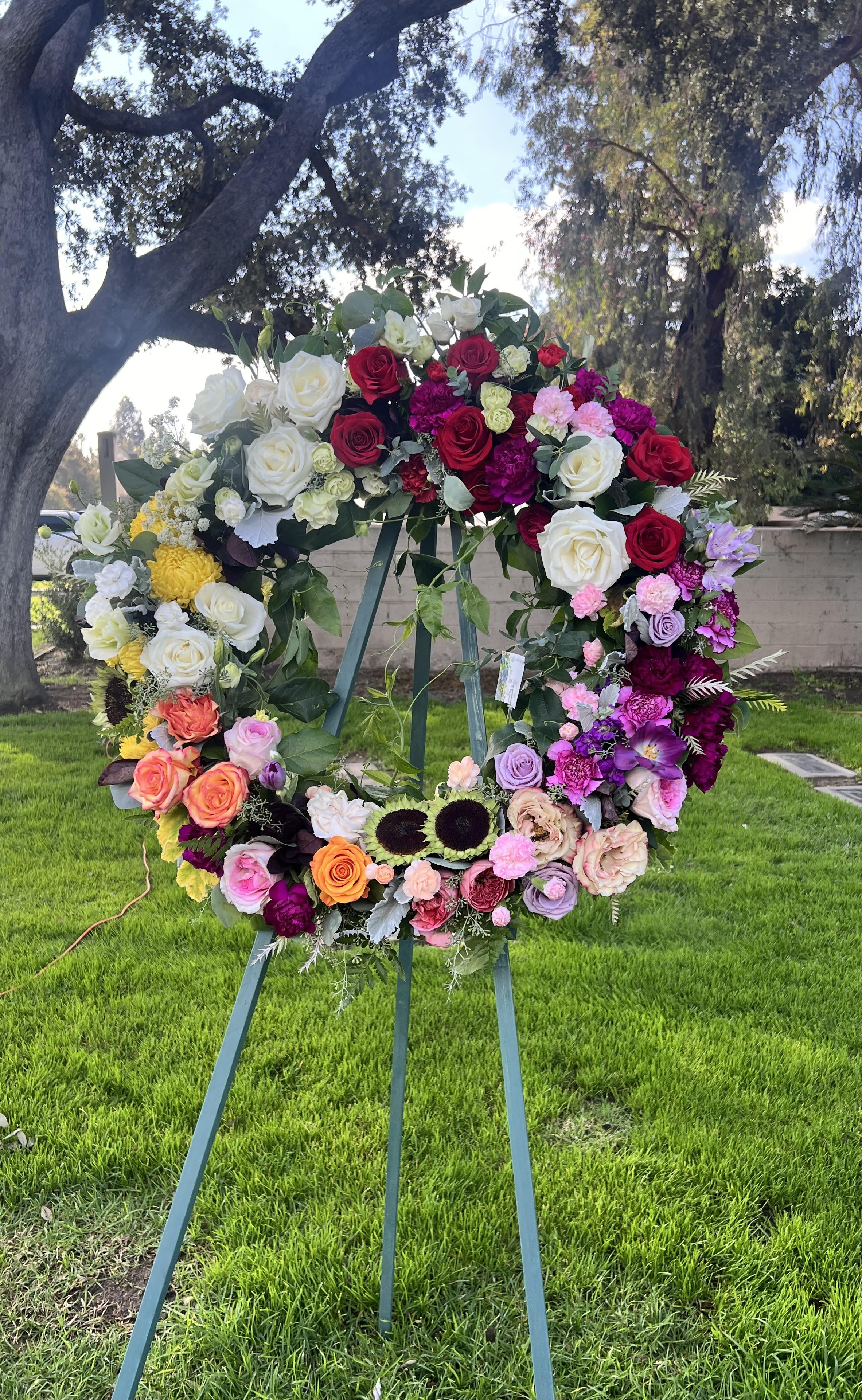 Large floral wreath on an easel with roses in red, white, pink, and purple