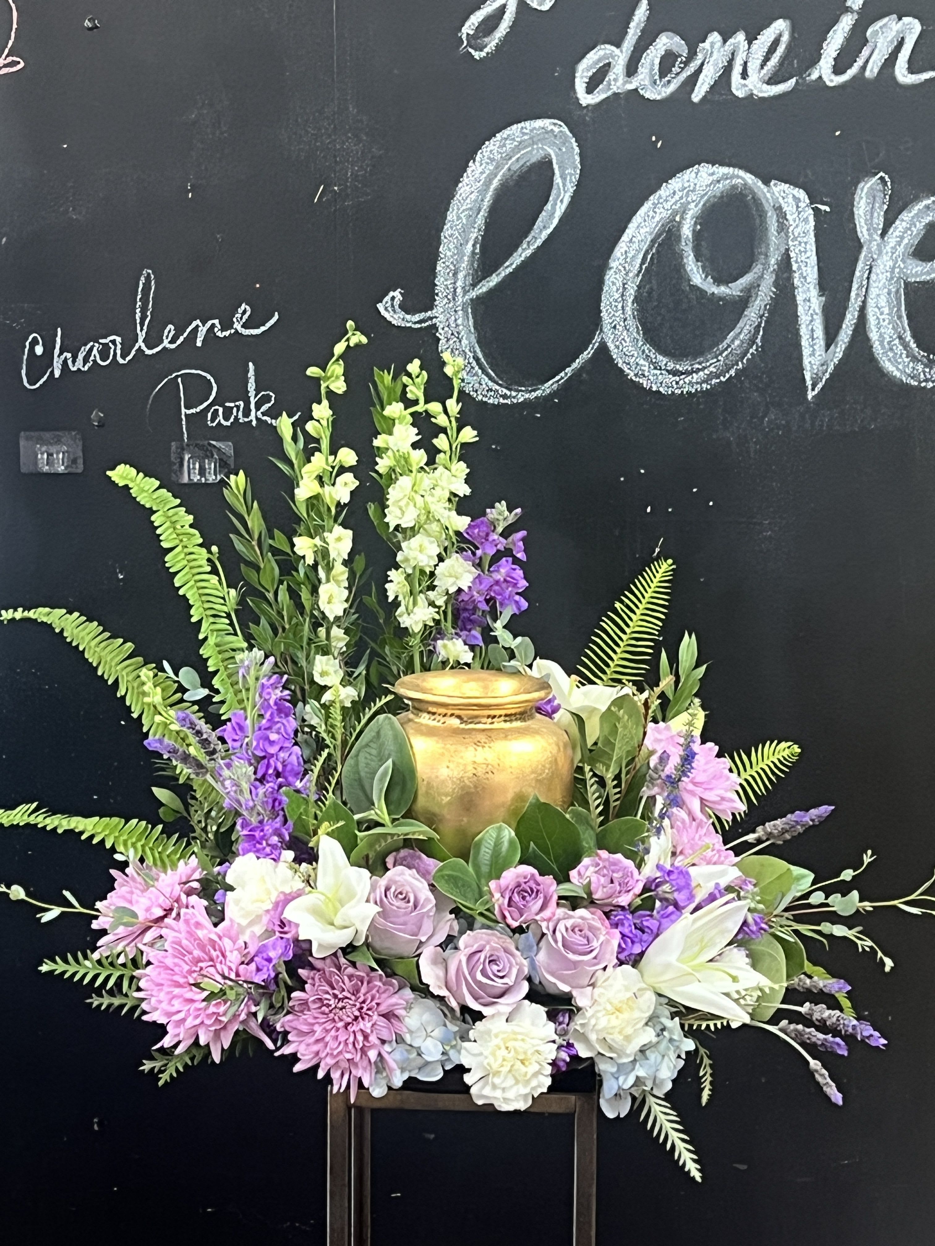 Lavender roses and pink flowers arranged around a gold urn