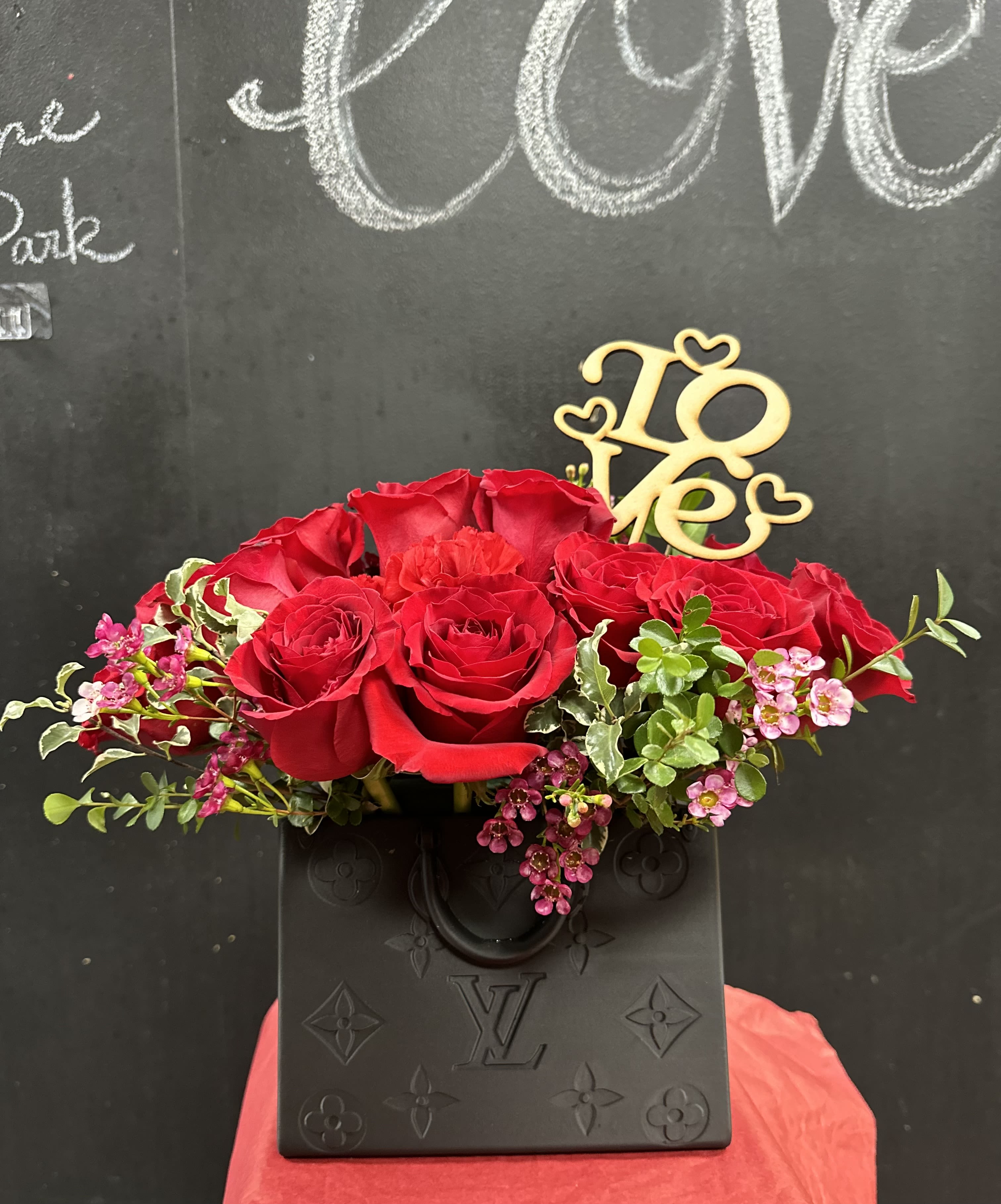Red roses arranged in a black vase with a gold "Love" topper.