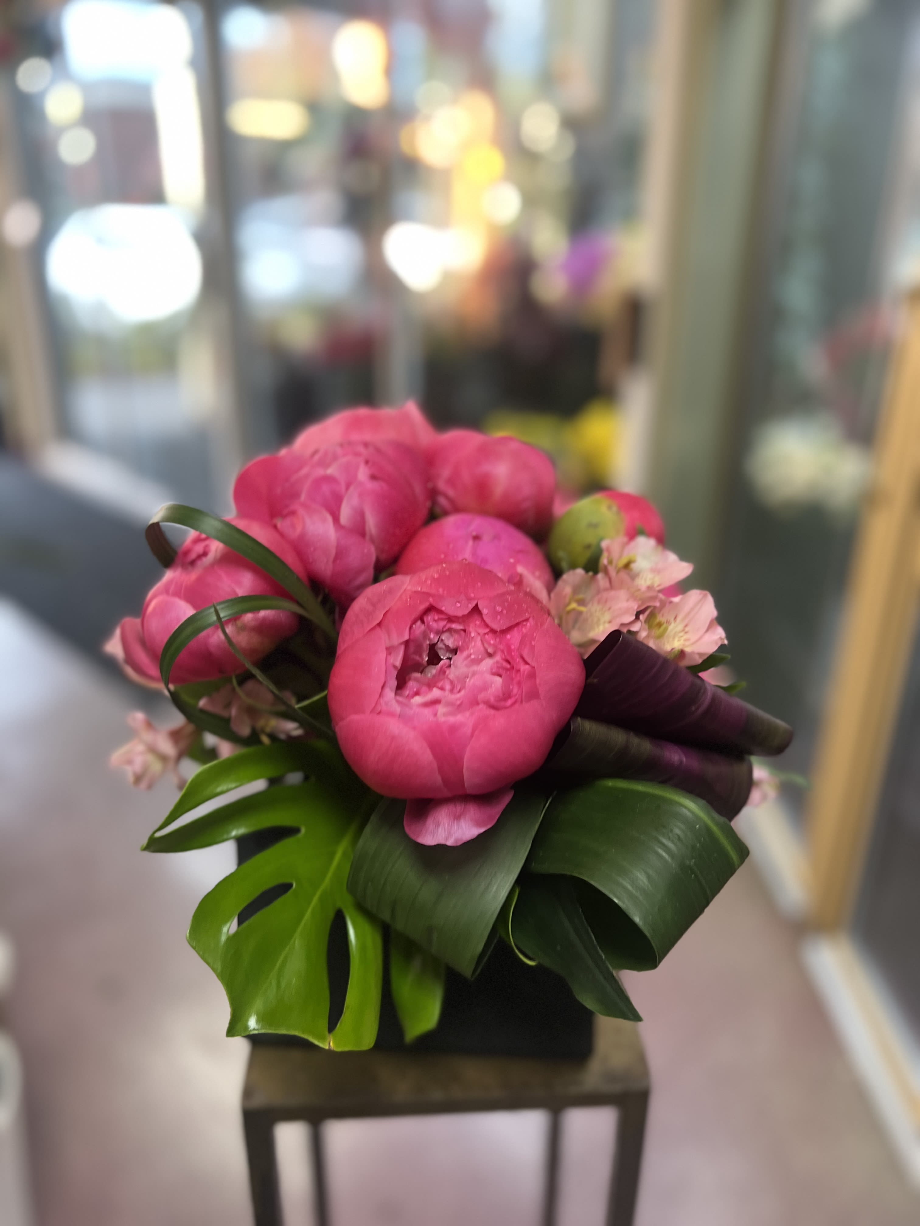 Pink peony bouquet with tropical leaves and small pale blossoms