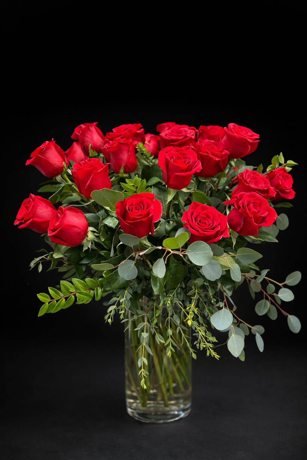 Red roses arranged in a clear glass vase with eucalyptus