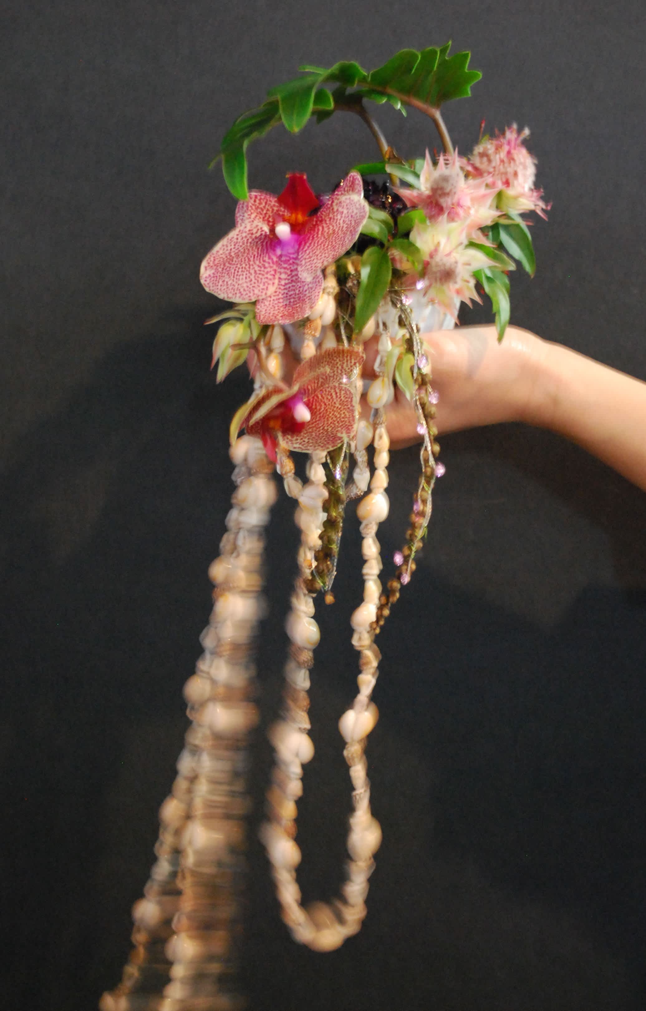 Handheld floral piece with pink orchids and hanging shells