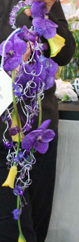 Purple orchid arrangement with silver curling ribbons and yellow calla lilies