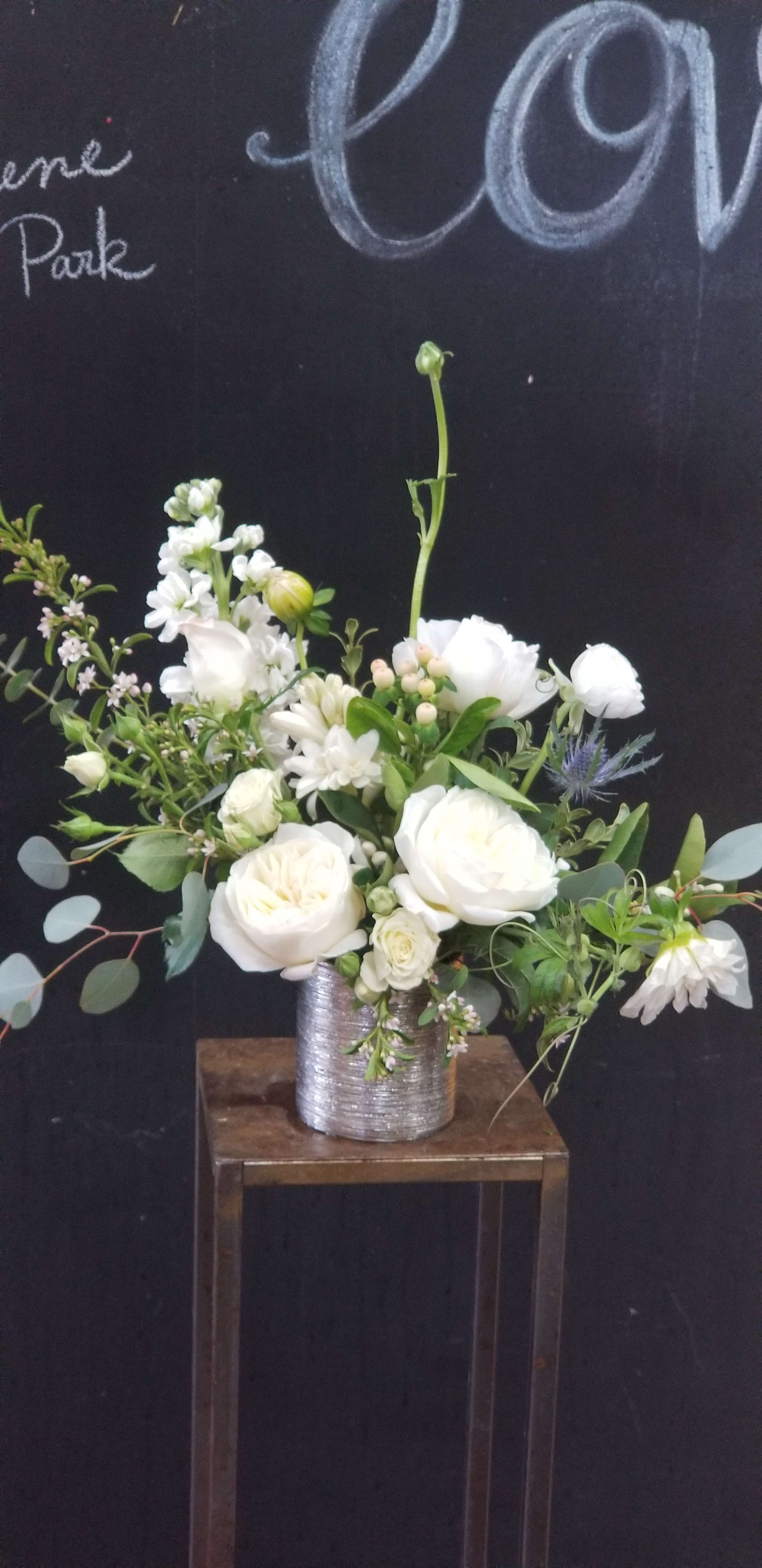 White floral arrangement in a silver vase on a wooden stand